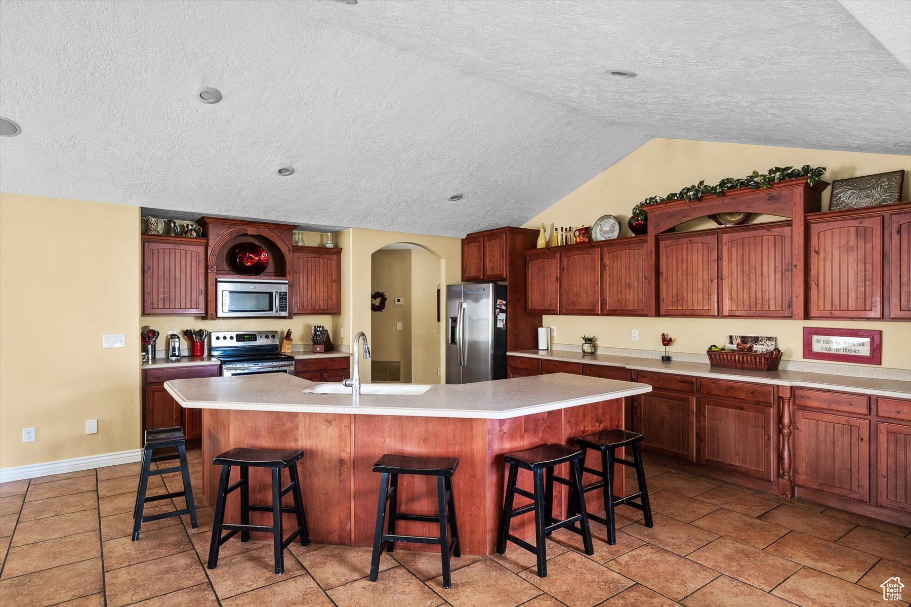 Kitchen with stainless steel appliances, a kitchen island with sink, vaulted ceiling, sink, and light tile floors