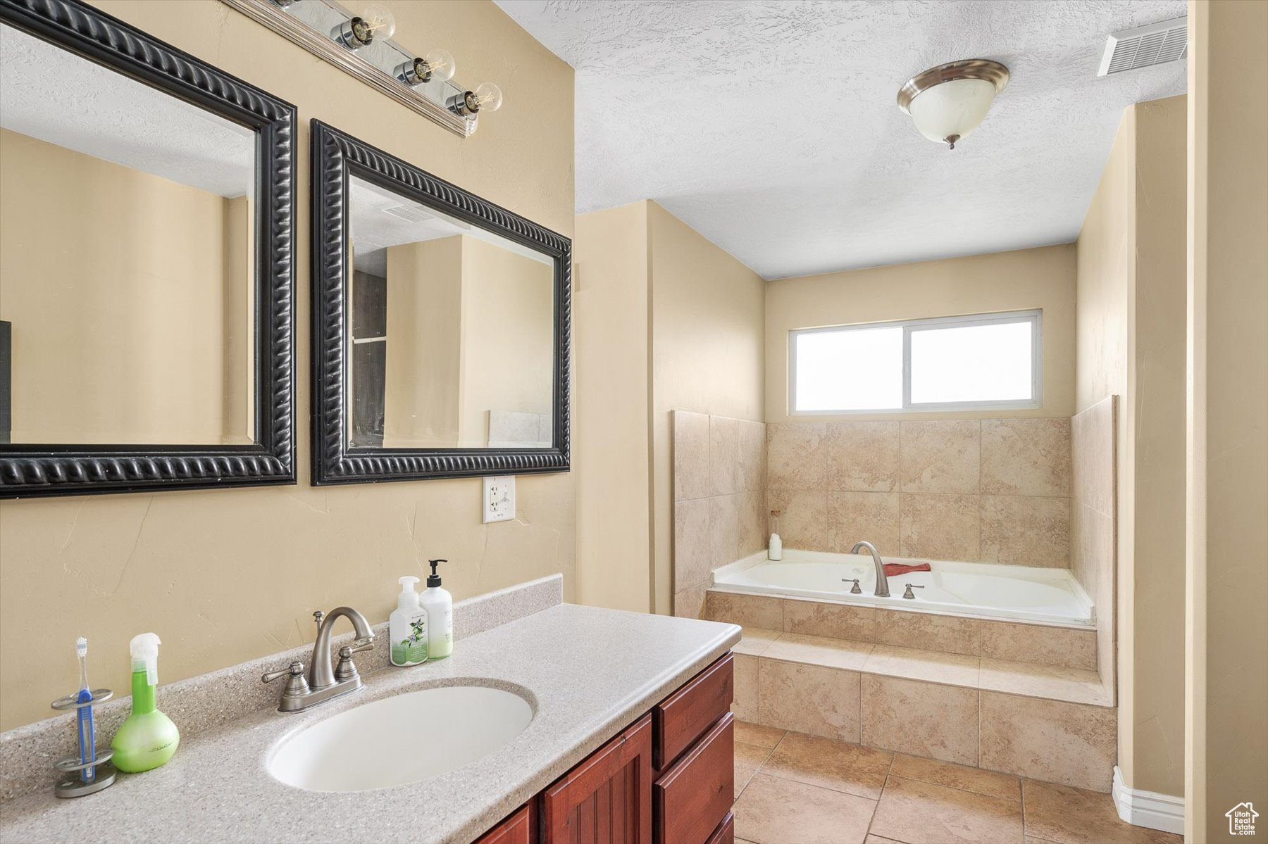 Bathroom featuring jetted soaking tub, tile floors, tiled bath, a textured ceiling, and vanity