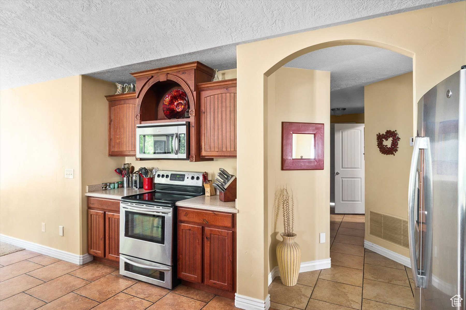 Kitchen with a textured ceiling, light tile floors, and appliances with stainless steel finishes