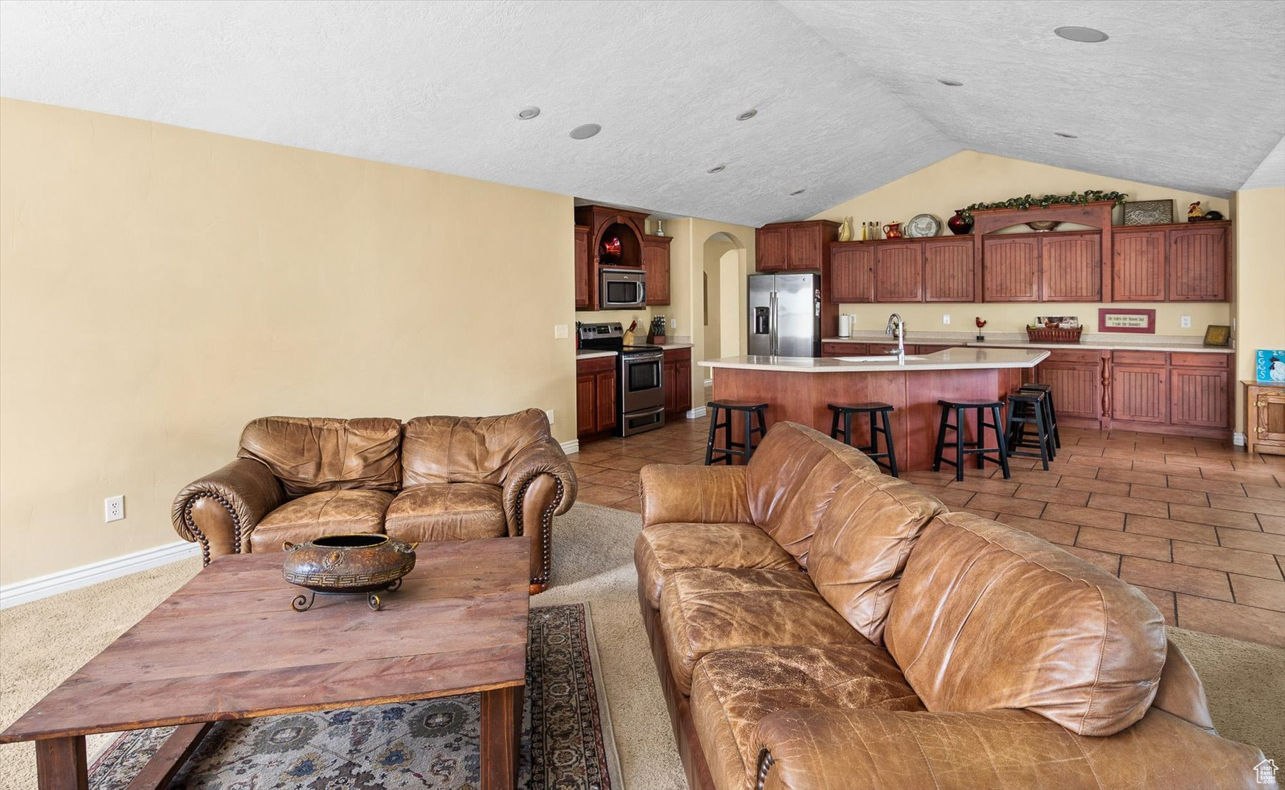 Living room featuring sink, vaulted ceiling, light tile floors, and a textured ceiling