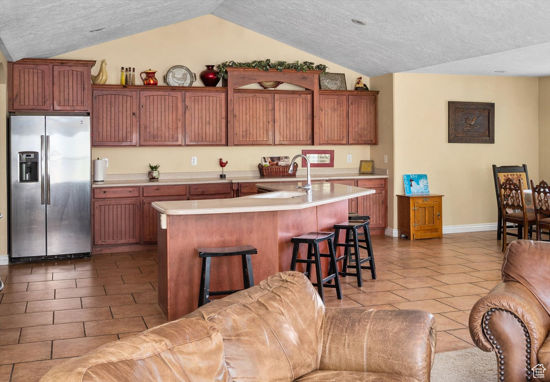 Kitchen with a kitchen breakfast bar, stainless steel refrigerator with ice dispenser, a textured ceiling, sink, and lofted ceiling