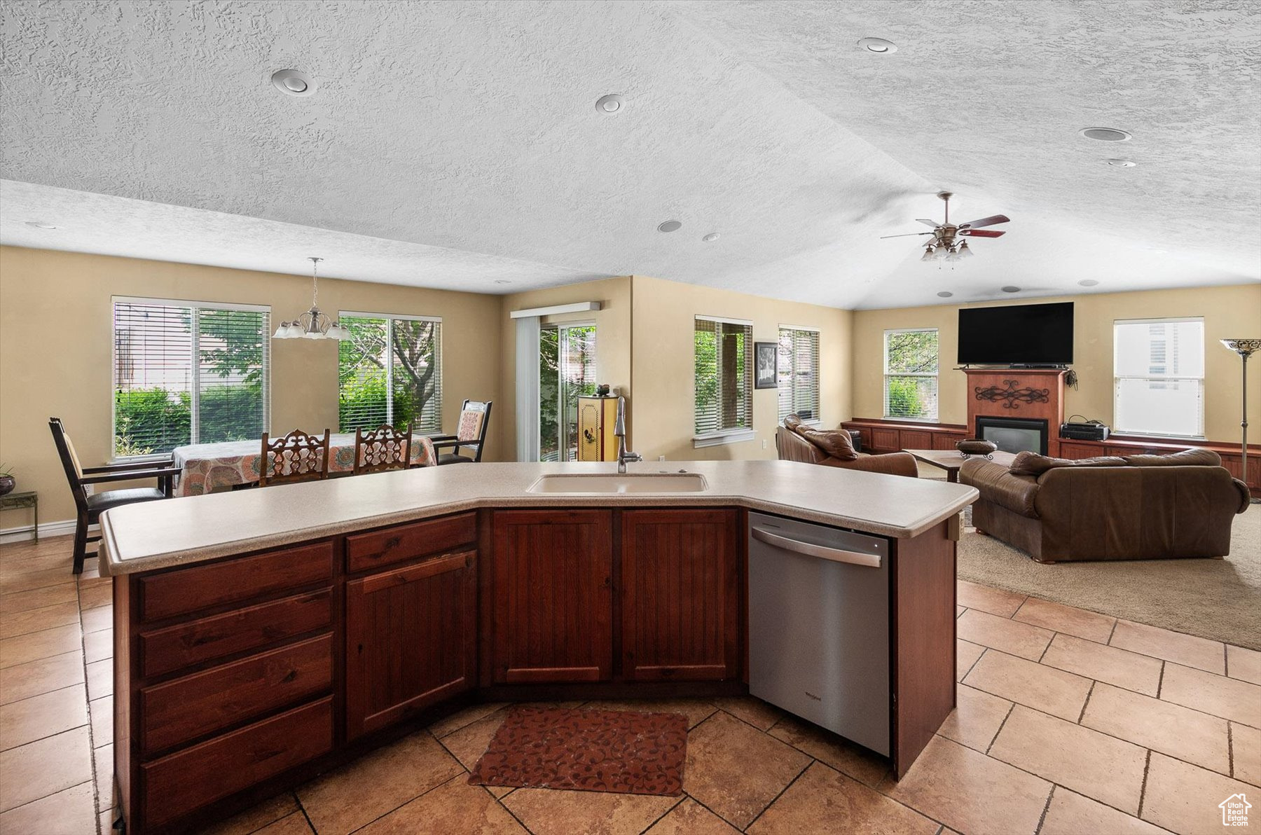 Kitchen with light tile flooring, a center island with sink, and stainless steel dishwasher