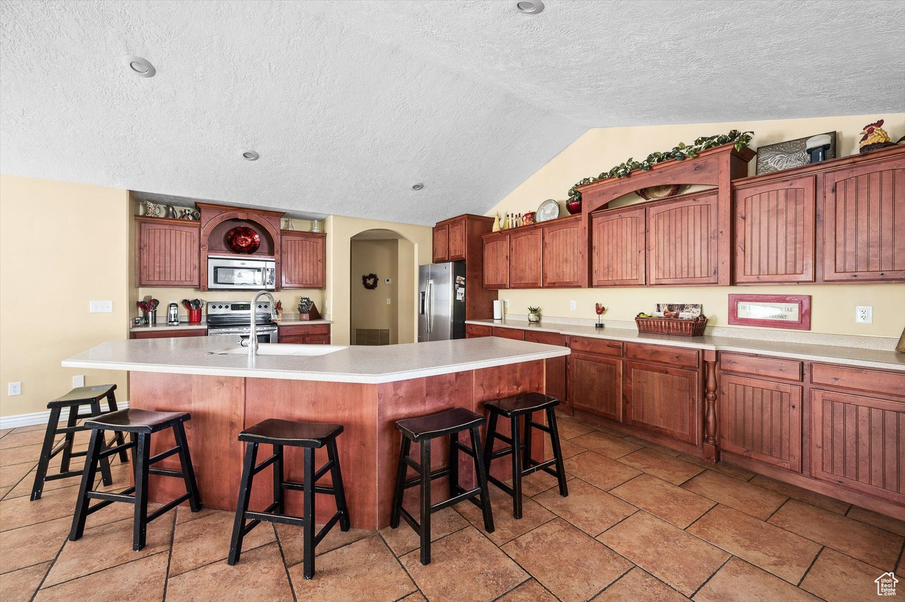 Kitchen with a center island with sink, light tile flooring, lofted ceiling, and appliances with stainless steel finishes