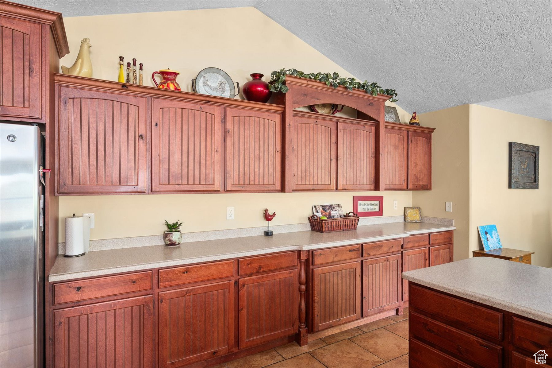 Kitchen featuring light tile flooring, a textured ceiling, stainless steel fridge, and vaulted ceiling