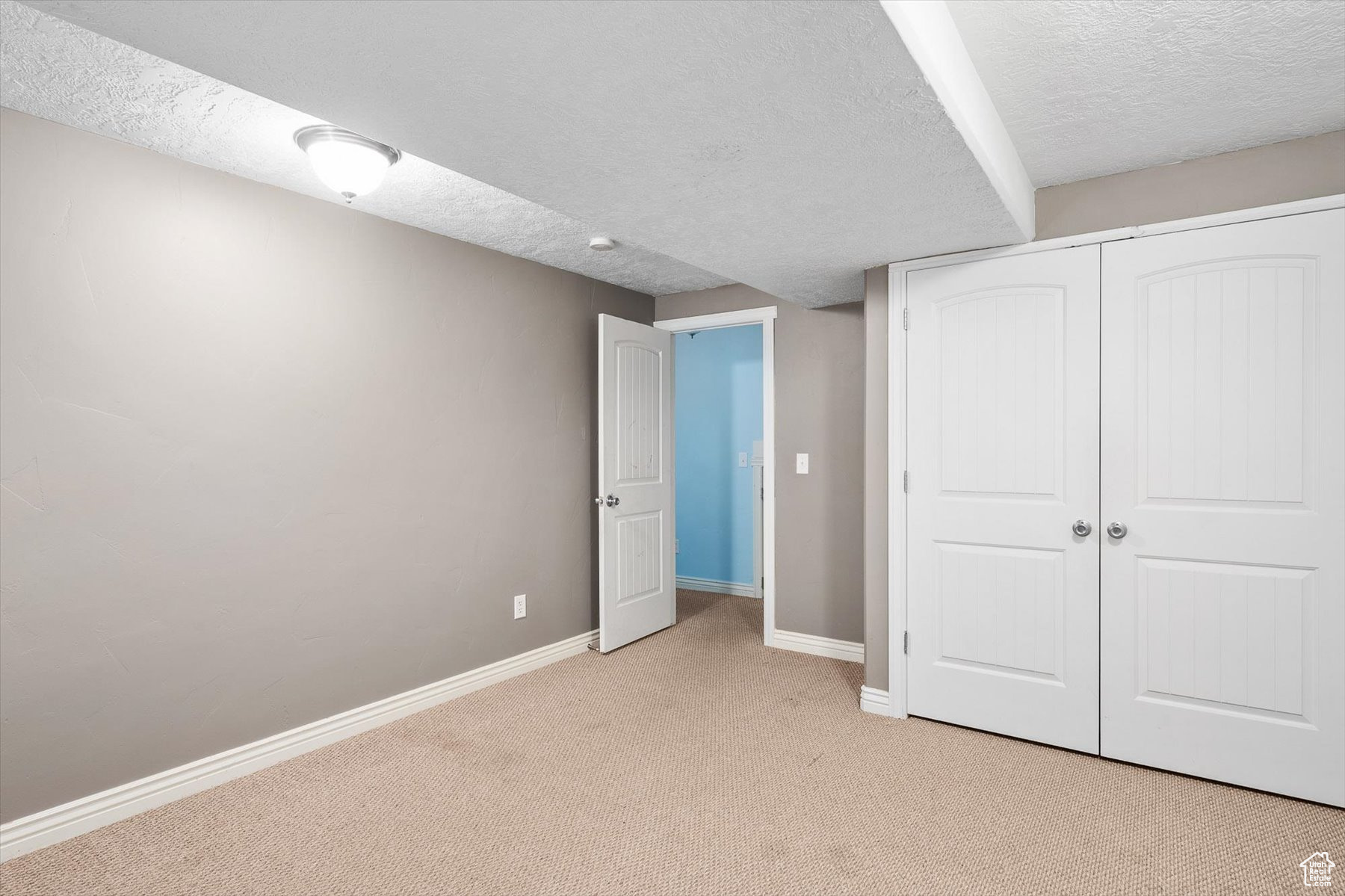 Unfurnished bedroom featuring a closet, a textured ceiling, and light colored carpet