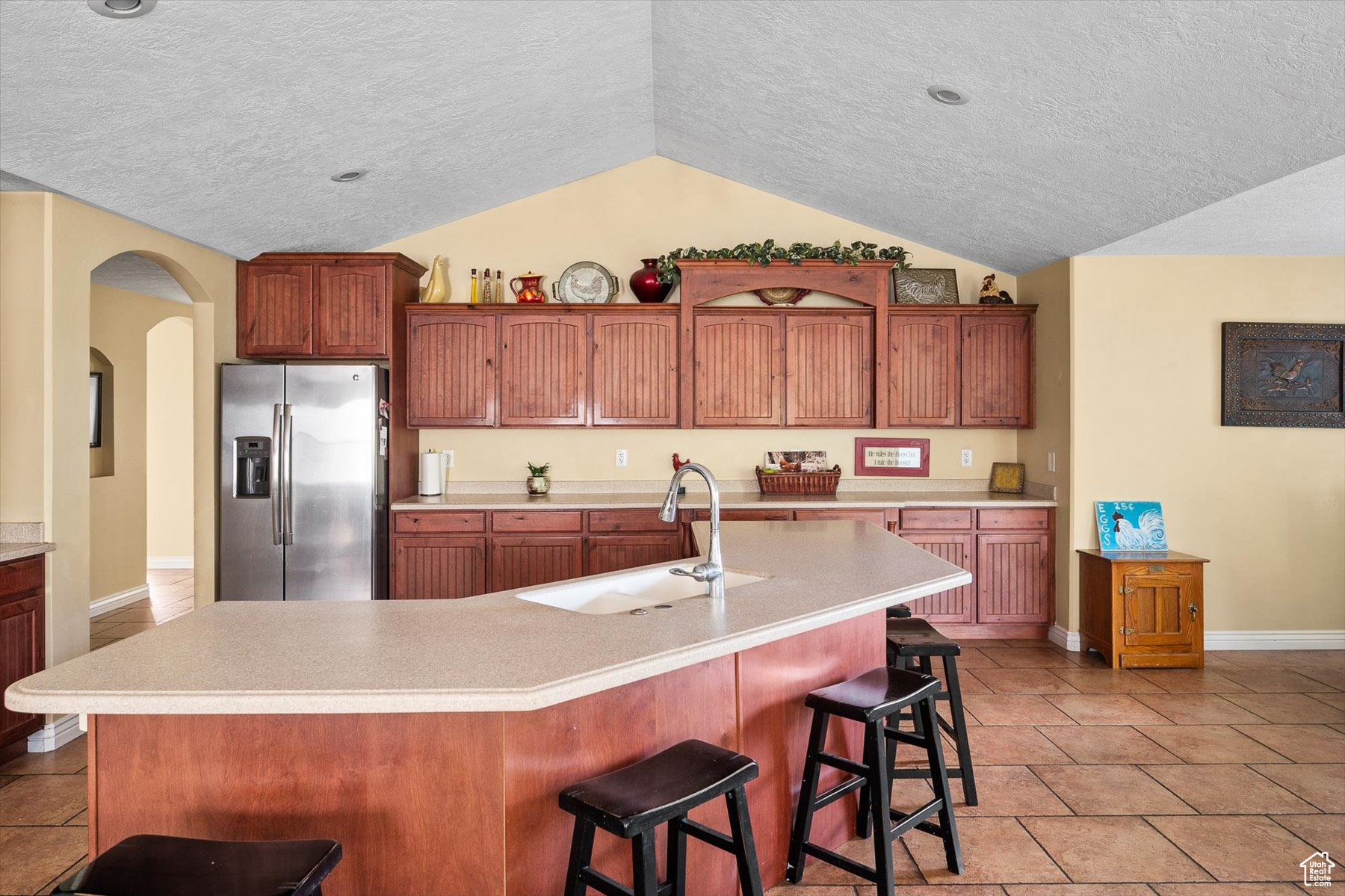 Look at all this Storage! Kitchen featuring vaulted ceiling, light tile flooring, an island with sink, stainless steel fridge, and sink