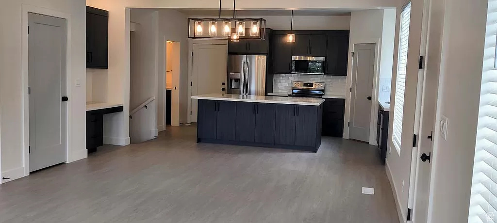 Kitchen with hanging light fixtures, a center island with sink, stainless steel appliances, backsplash, and wood-type flooring