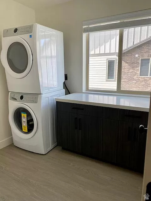 Washroom with stacked washer / drying machine, light hardwood / wood-style floors, and a wealth of natural light