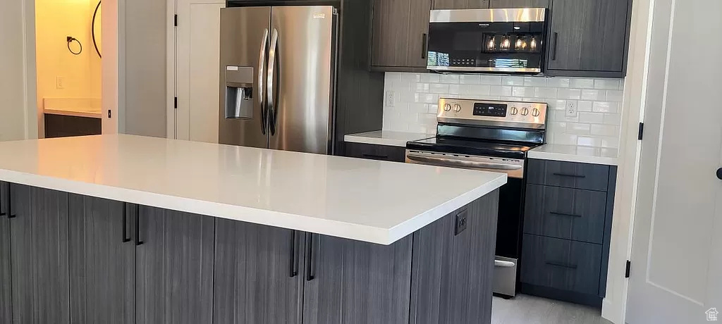 Kitchen featuring a center island, light wood-type flooring, backsplash, and appliances with stainless steel finishes