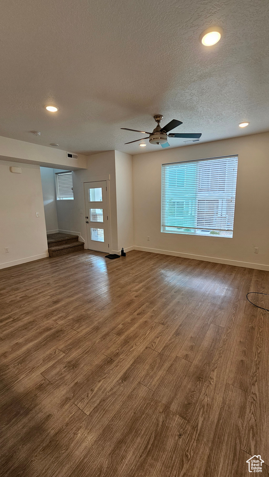 Living room with ceiling fan, a textured ceiling, and light wood-type flooring