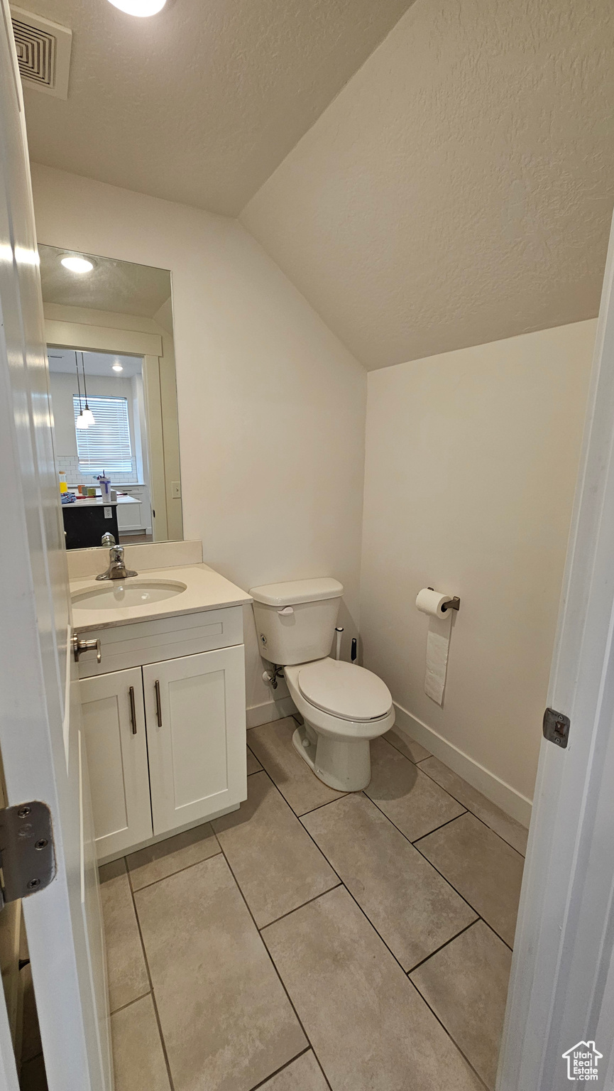 Bathroom with tile flooring, oversized vanity, lofted ceiling, and toilet