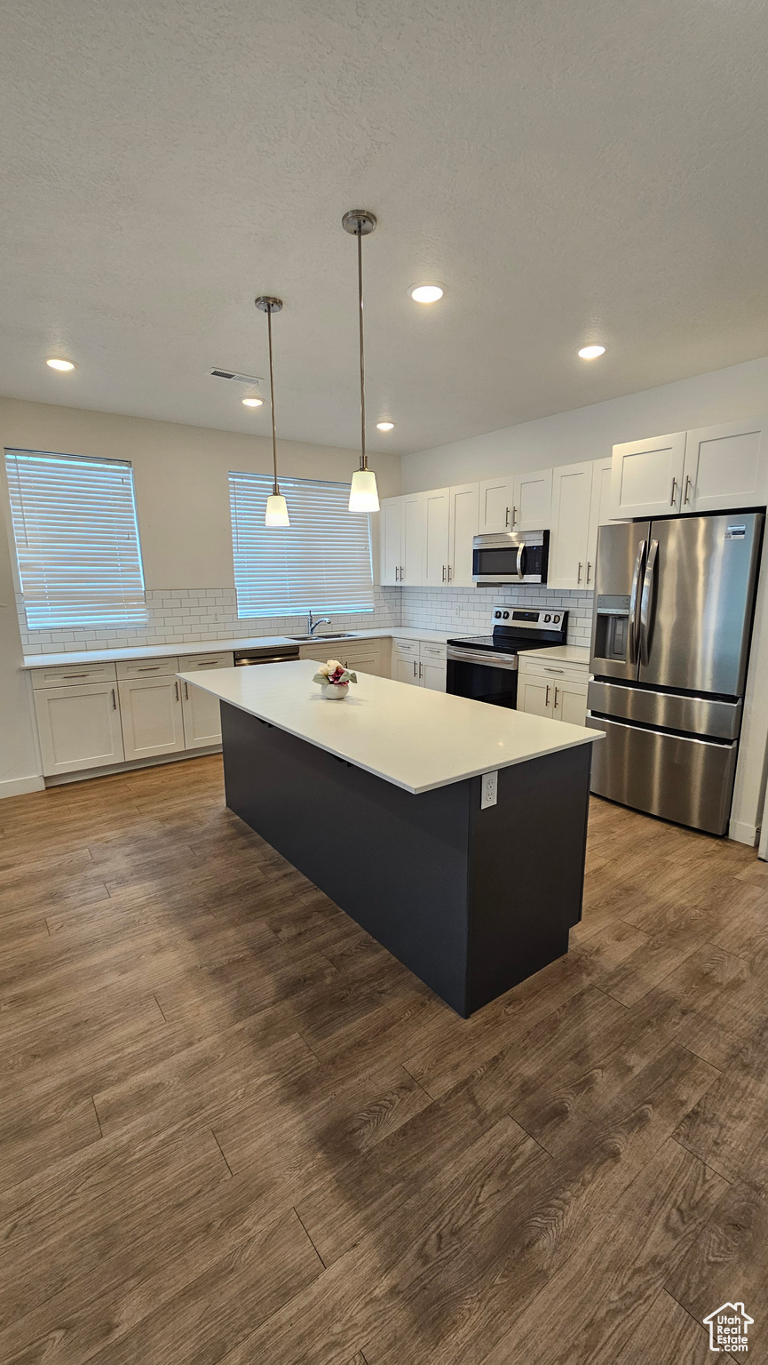 Kitchen with a center island, stainless steel appliances, white cabinets, and wood-type flooring