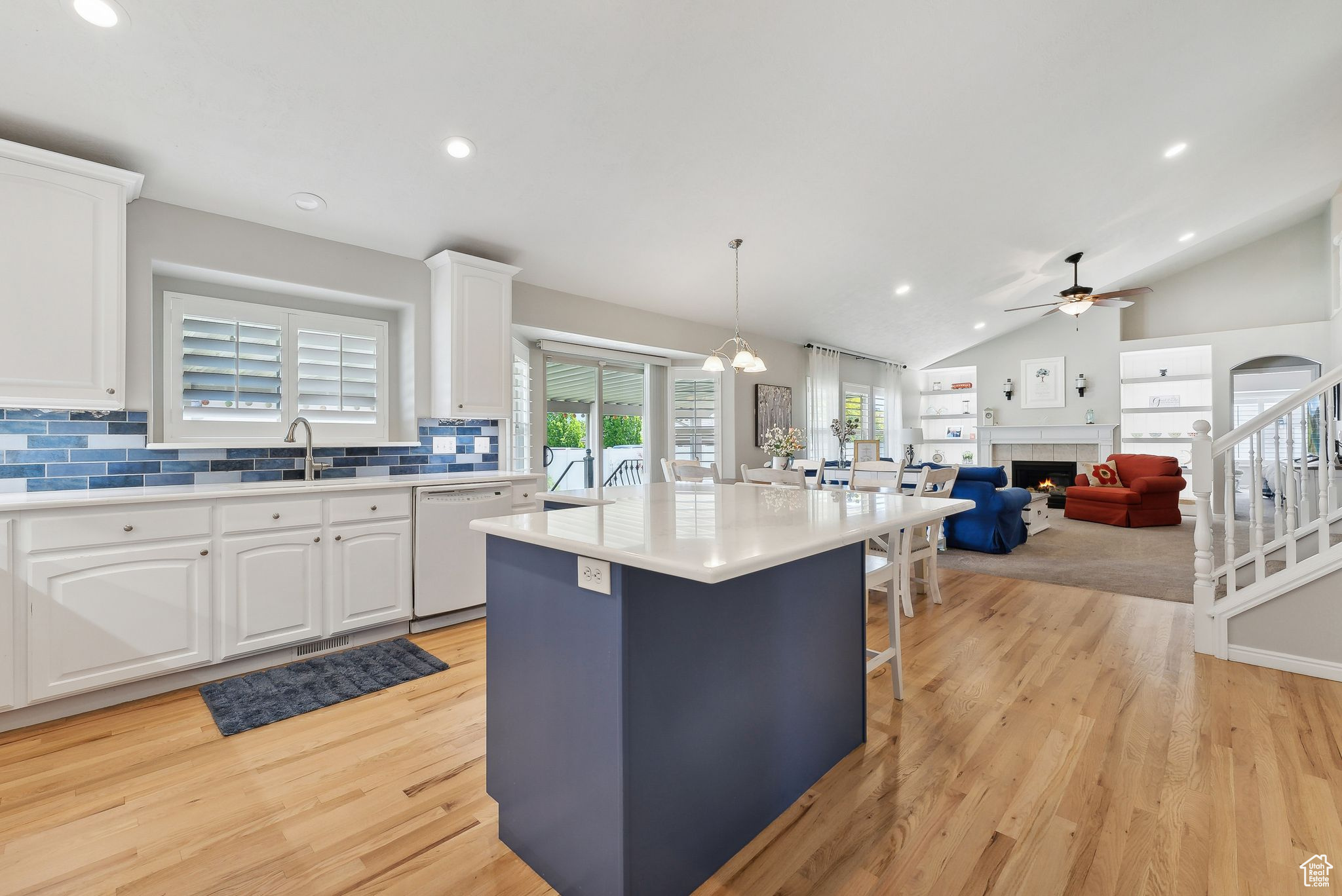 Kitchen with a tiled fireplace, light hardwood / wood-style floors, dishwasher, a center island, and white cabinets