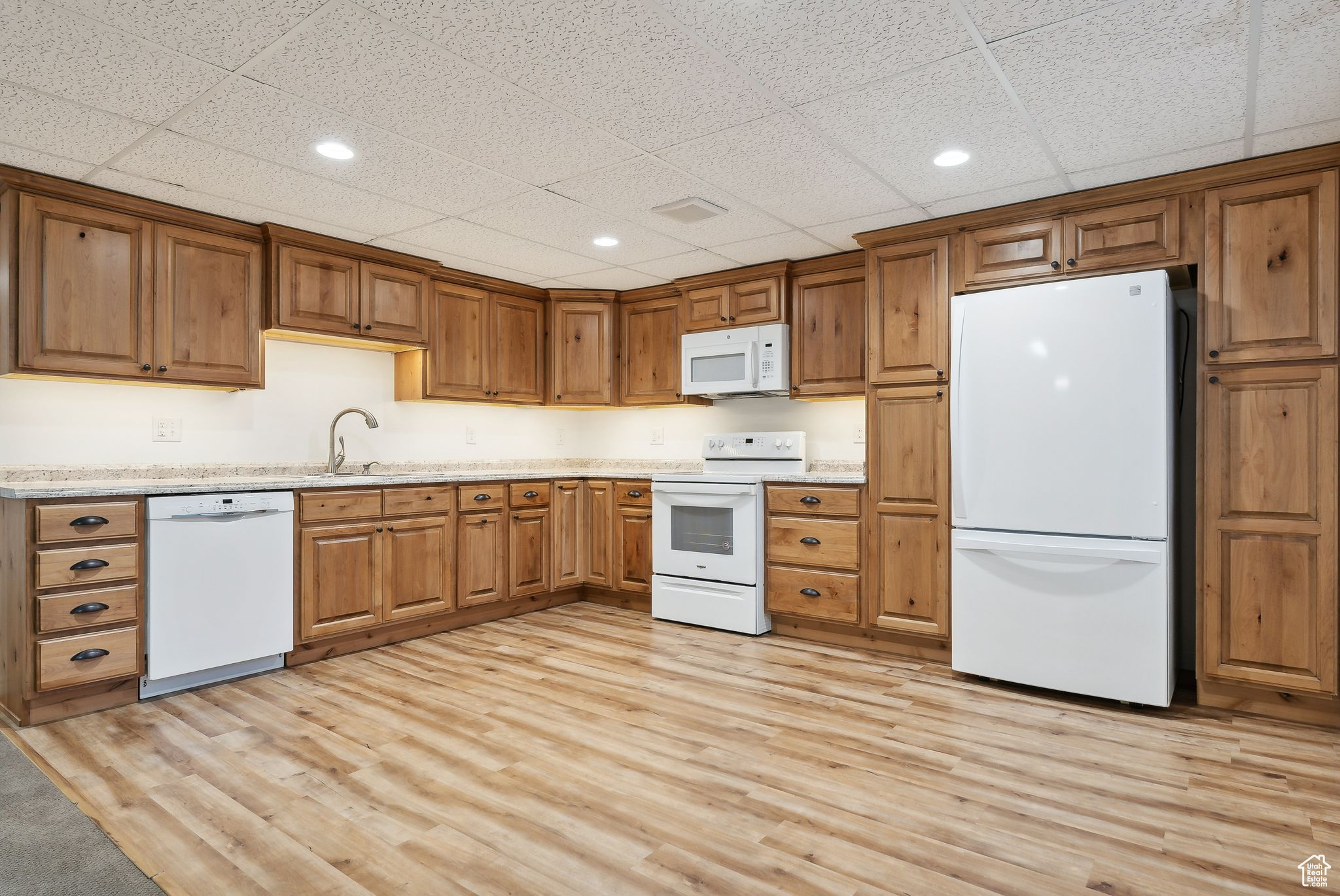 Kitchen featuring light hardwood / wood-style floors, sink, white appliances, and a drop ceiling