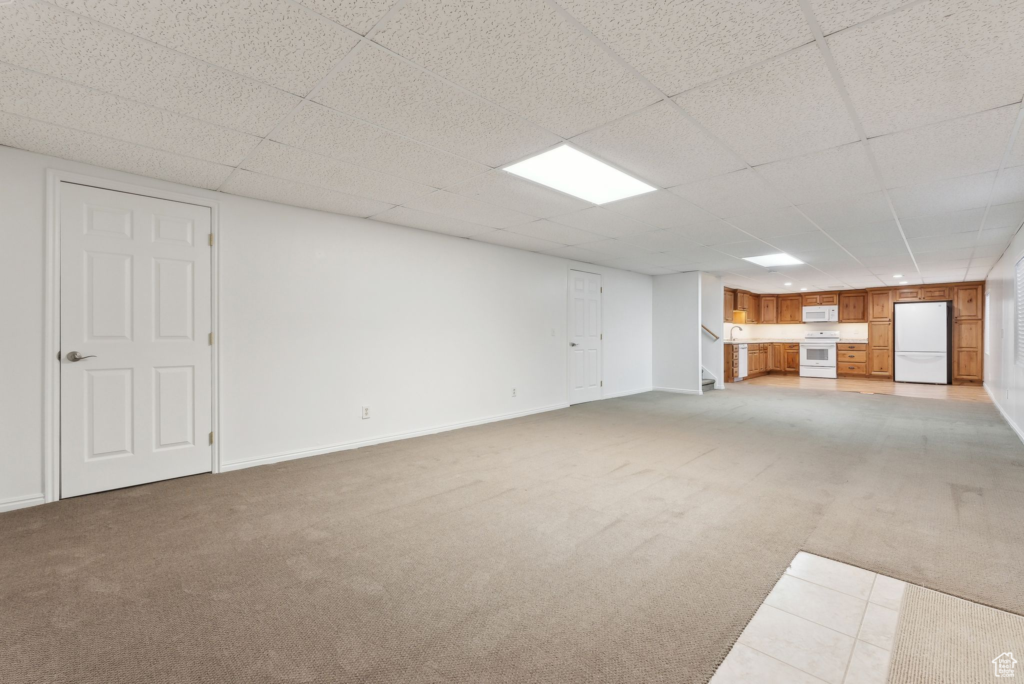 Basement featuring white refrigerator, a paneled ceiling, and carpet floors