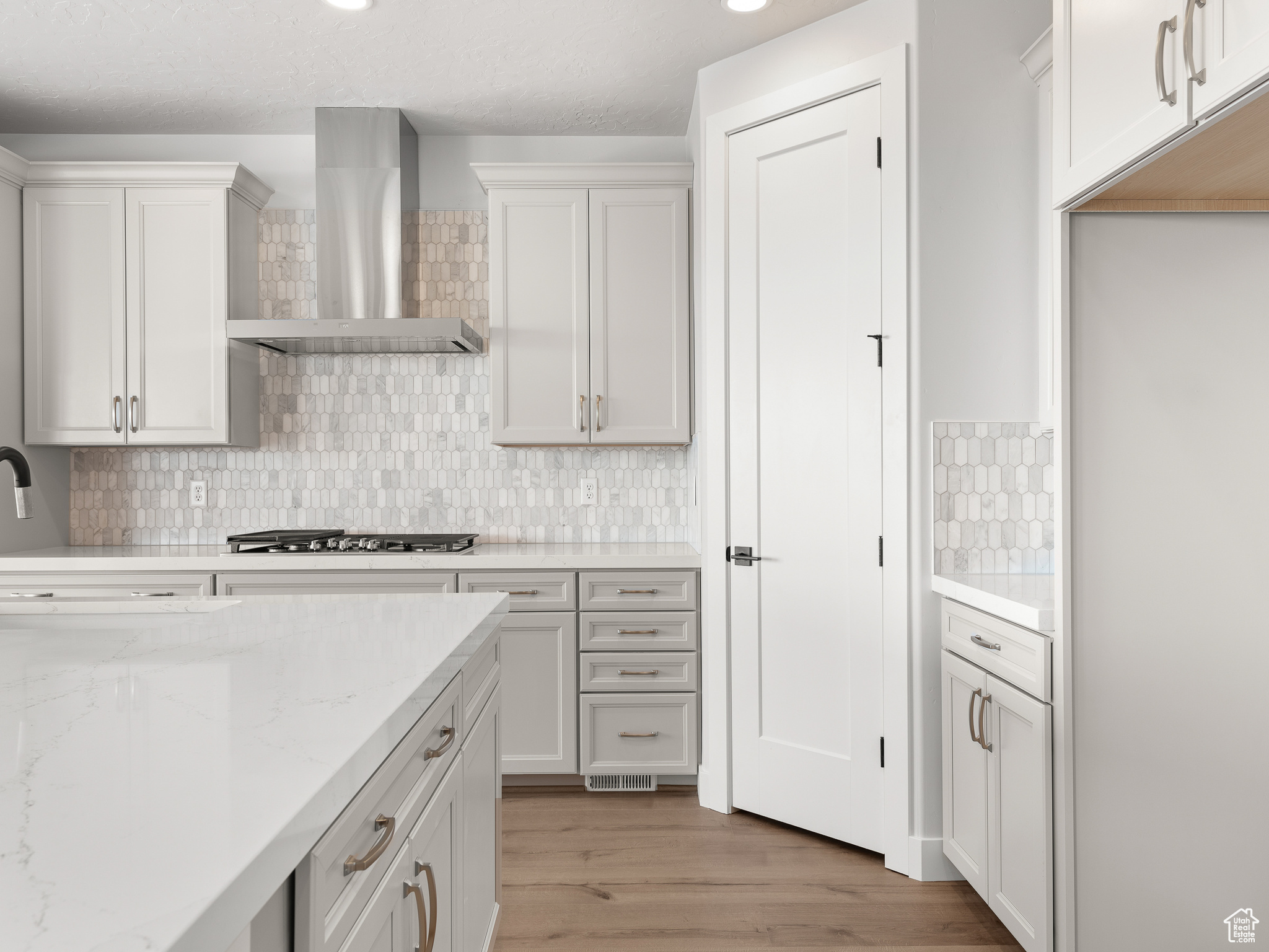 Kitchen featuring stainless steel gas cooktop, backsplash, hardwood / wood-style flooring, light stone countertops, and wall chimney exhaust hood. This is a picture of Helena model home. Not the interior of actual home.