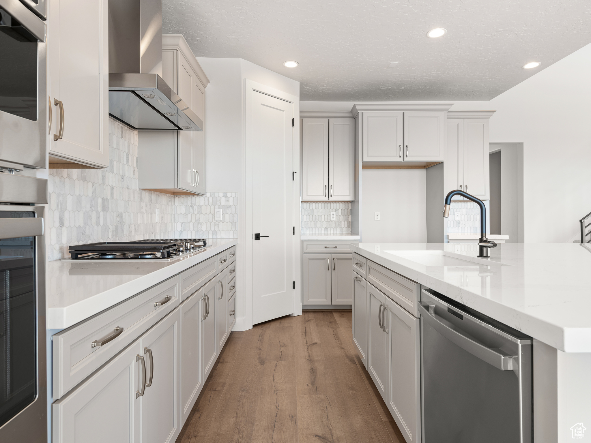 Kitchen with stainless steel appliances, backsplash, wall chimney exhaust hood, hardwood / wood-style flooring, and sink. This is a picture of Helena model home. Not the interior of actual home.