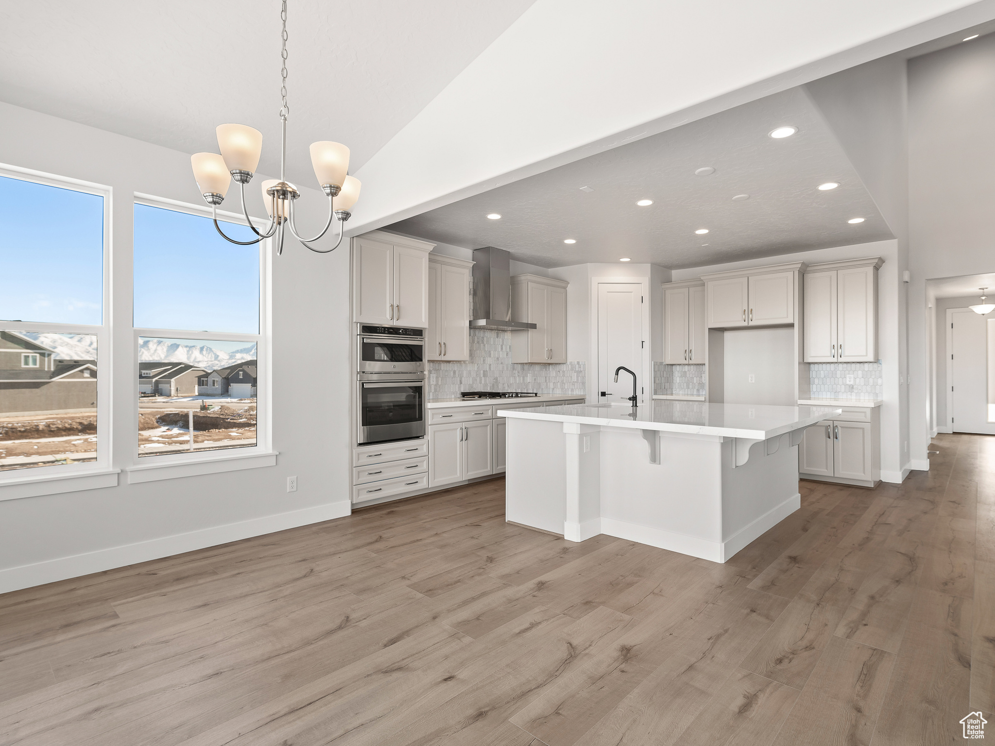 Kitchen with a kitchen island with sink, hardwood / wood-style flooring, and wall chimney exhaust hood. This is a picture of Helena model home. Not the interior of actual home.