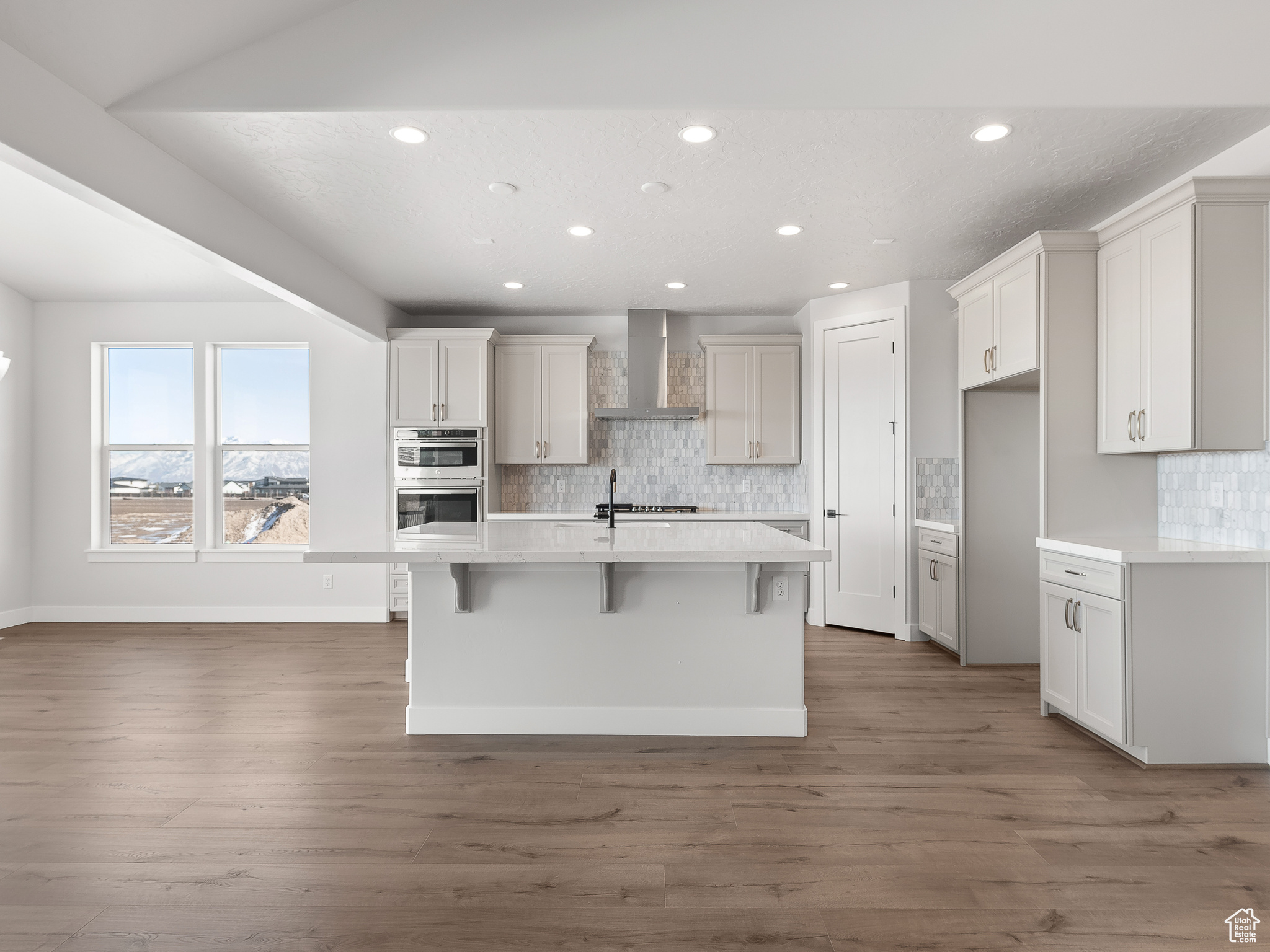 Kitchen with hardwood / wood-style flooring, backsplash, a center island with sink, and wall chimney exhaust hood. This is a picture of Helena model home. Not the interior of actual home.