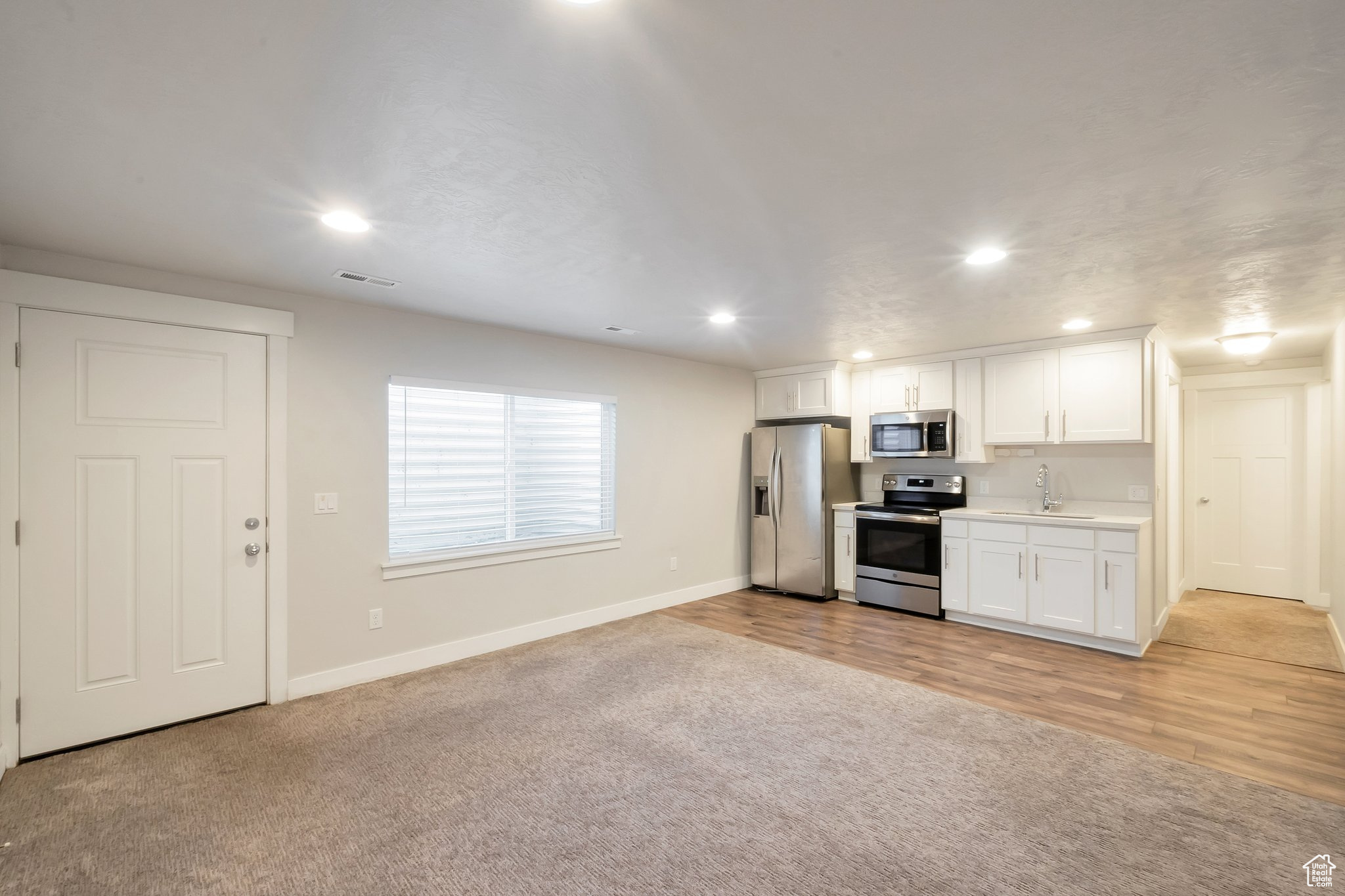 Kitchen featuring light carpet, sink, white cabinets, and appliances with stainless steel finishes