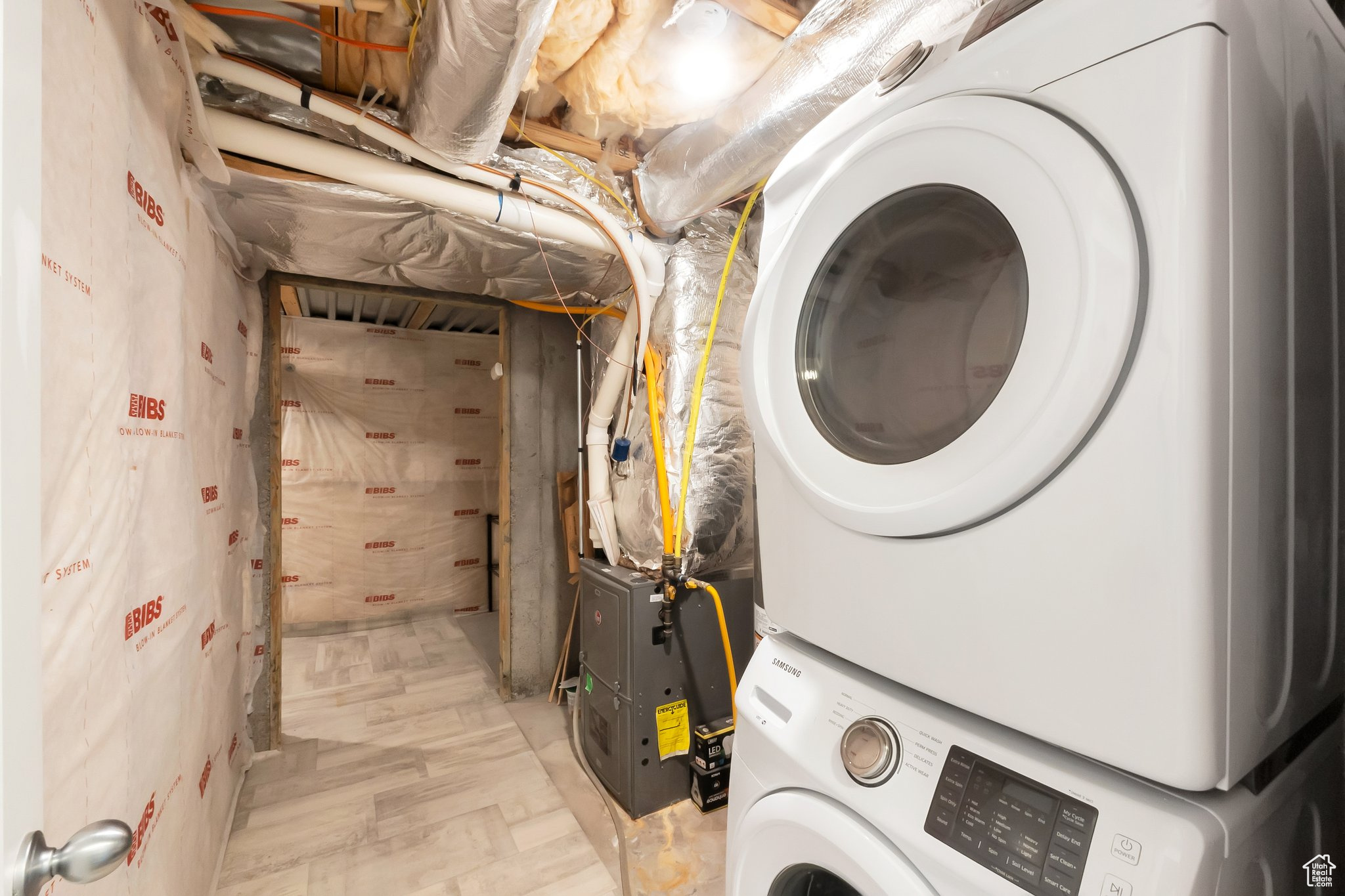 Washroom with stacked washer / dryer and light wood-type flooring