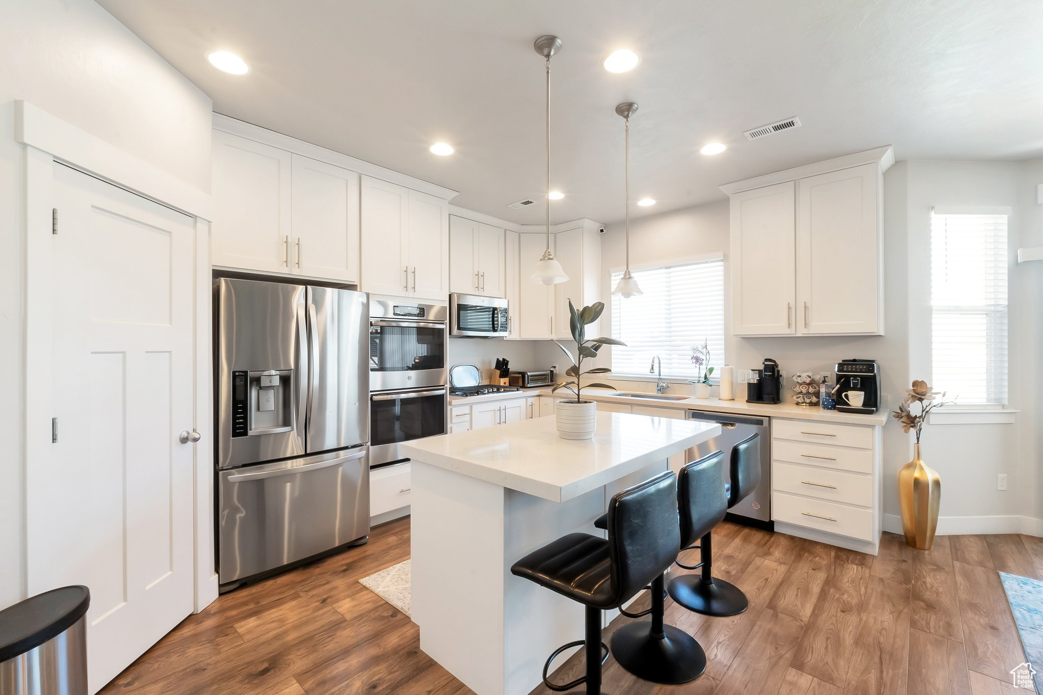 Kitchen with pendant lighting, sink, hardwood / wood-style flooring, white cabinetry, and appliances with stainless steel finishes