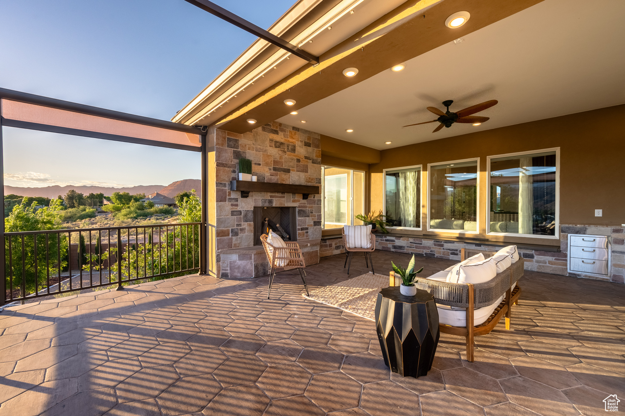 Patio terrace at dusk with an outdoor stone fireplace and ceiling fan