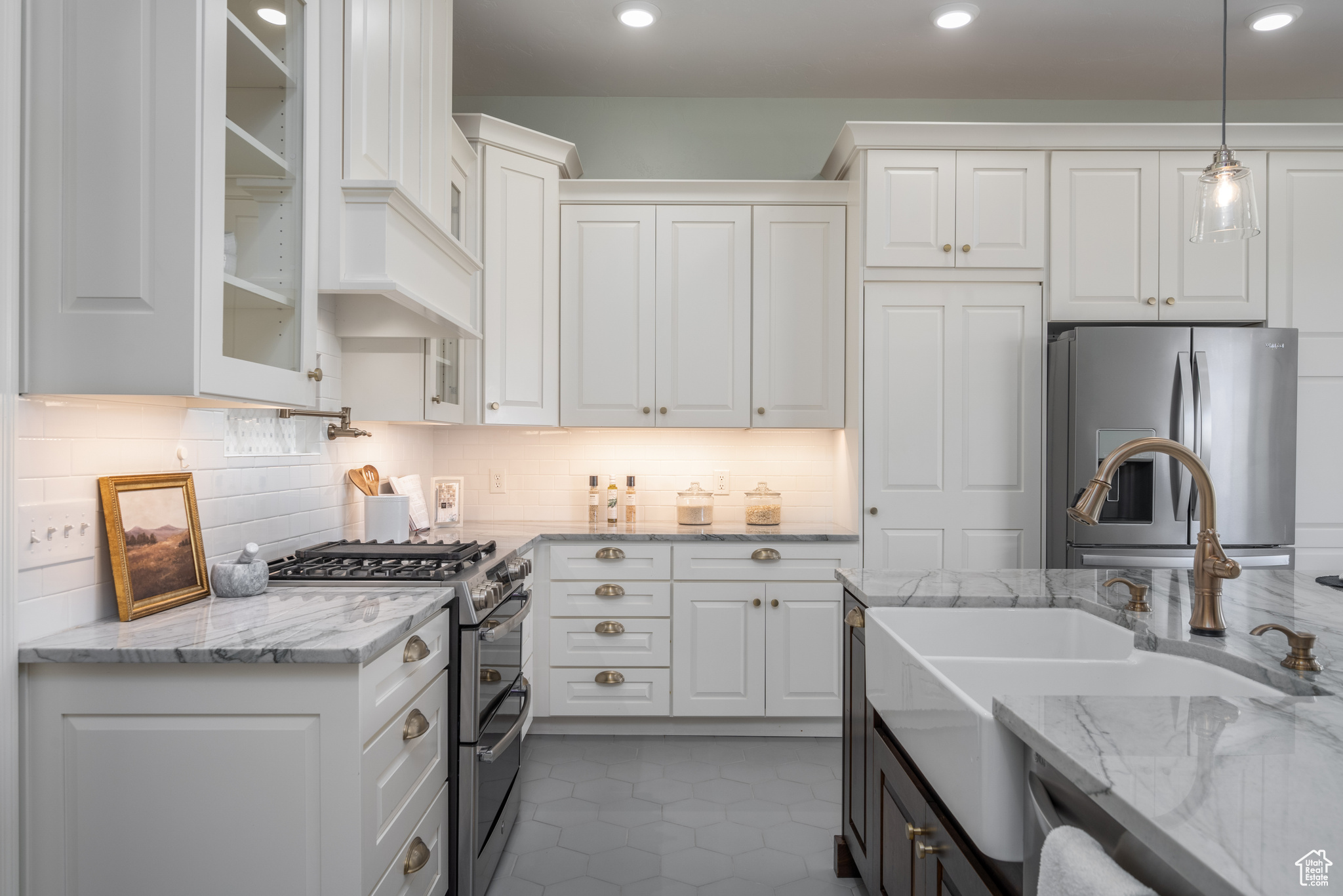 Kitchen with tasteful backsplash, decorative light fixtures, tile floors, white cabinetry, and appliances with stainless steel finishes