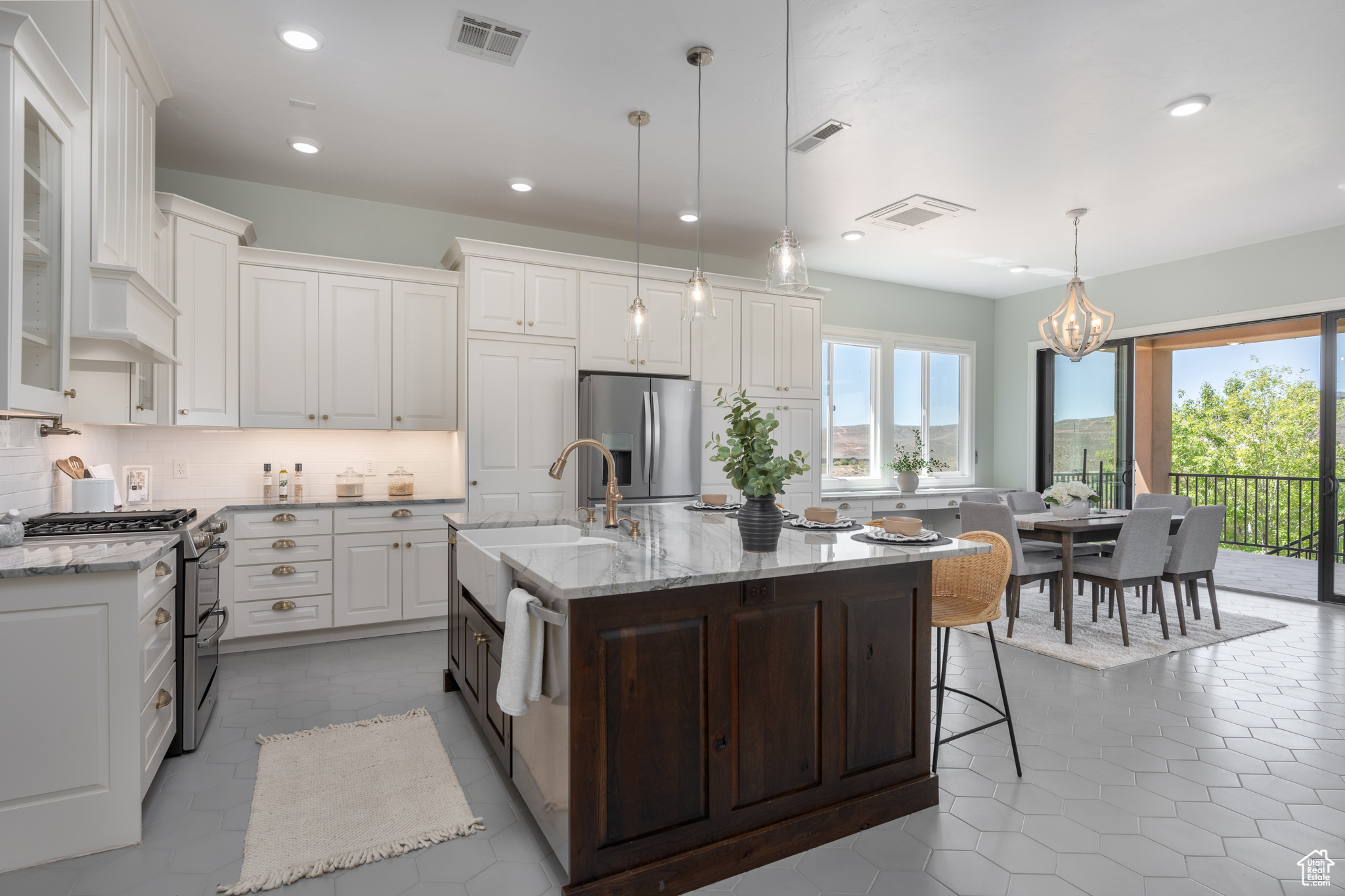 Kitchen featuring decorative light fixtures, stainless steel appliances, tasteful backsplash, tile floors, and a kitchen island with sink