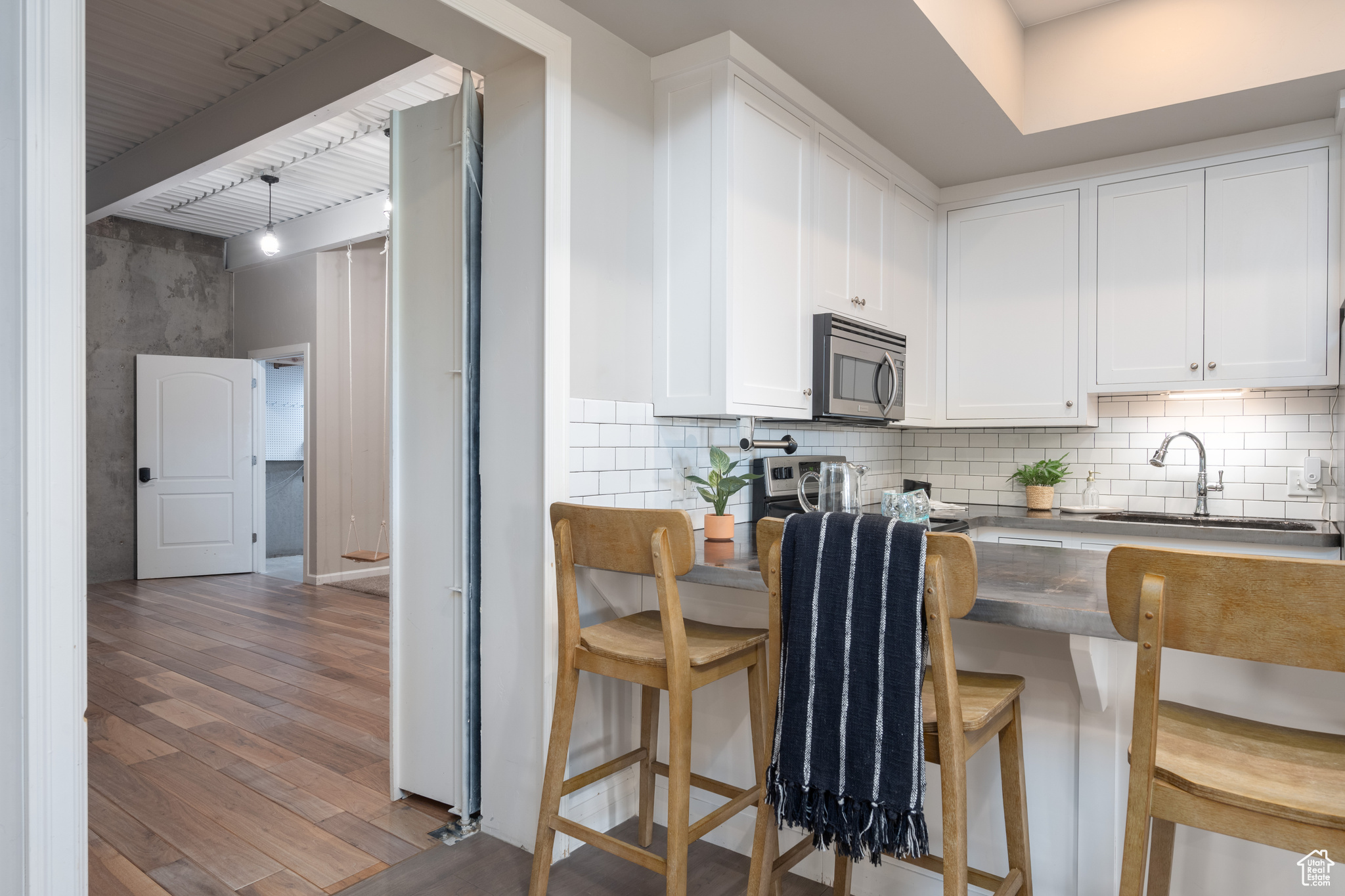 Kitchen featuring dark wood-type flooring, white cabinets, sink, tasteful backsplash, and a kitchen bar