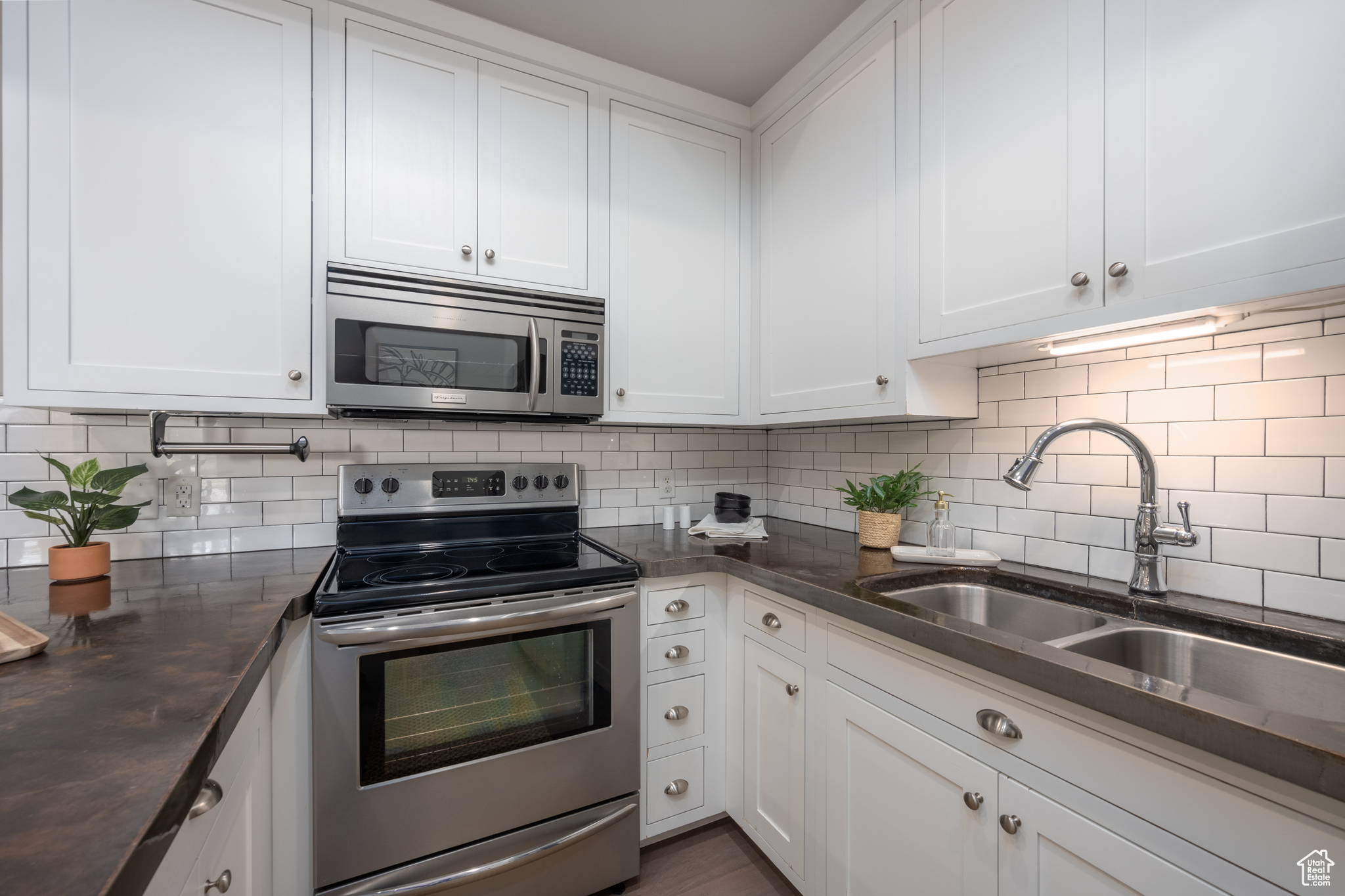 Kitchen with stainless steel appliances, white cabinets, backsplash, and sink