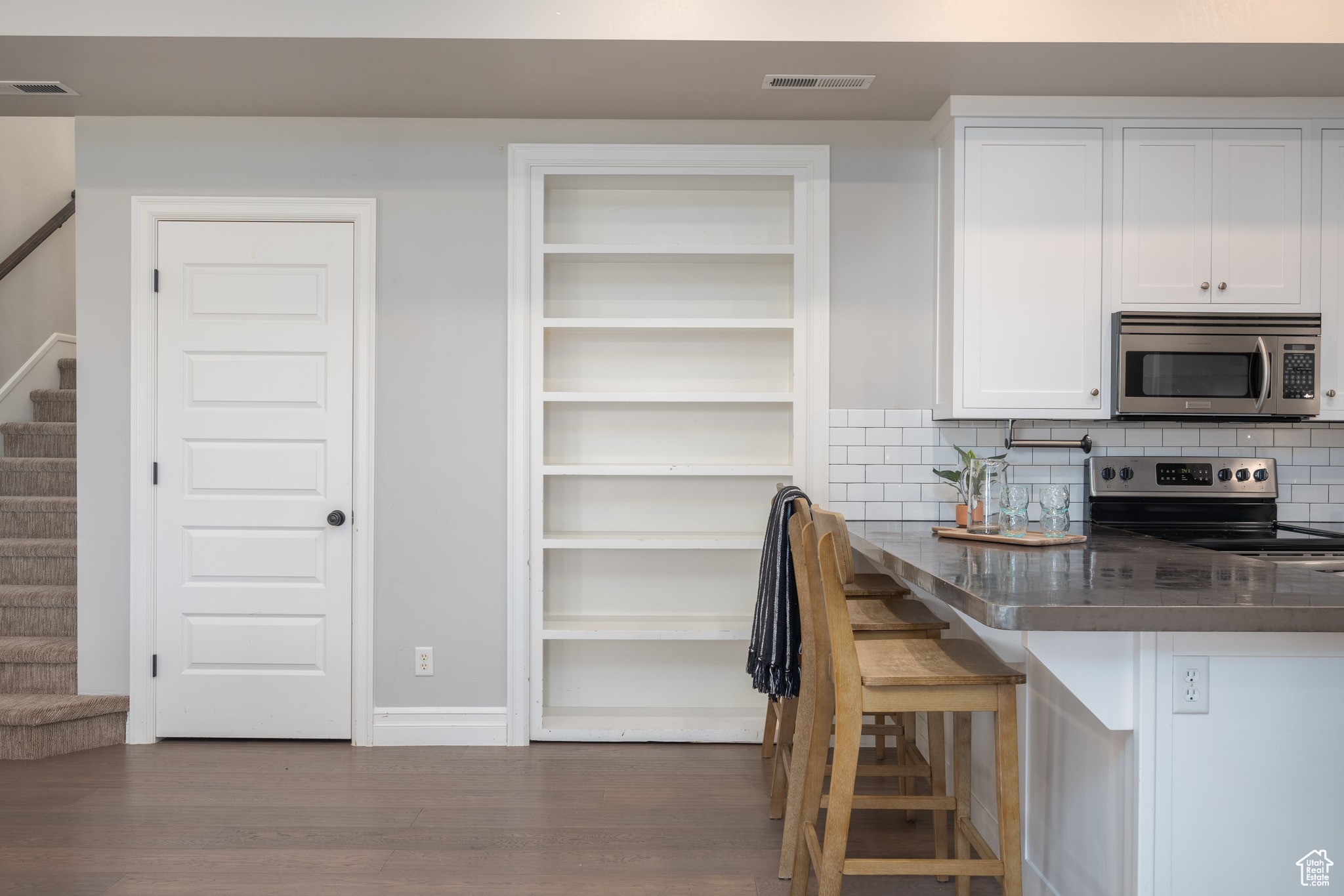 Kitchen featuring appliances with stainless steel finishes, white cabinets, dark hardwood / wood-style floors, backsplash, and a breakfast bar