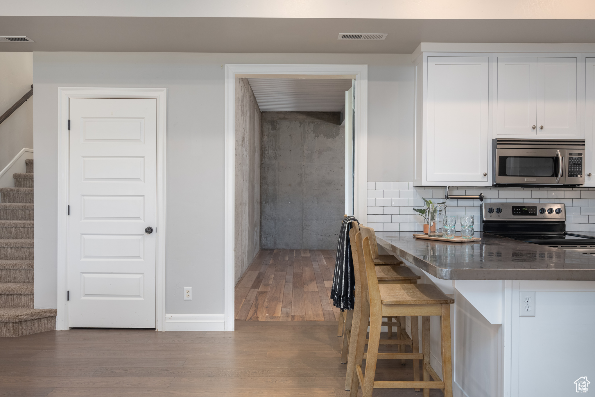 Kitchen with a kitchen breakfast bar, appliances with stainless steel finishes, white cabinets, hardwood / wood-style floors, and backsplash