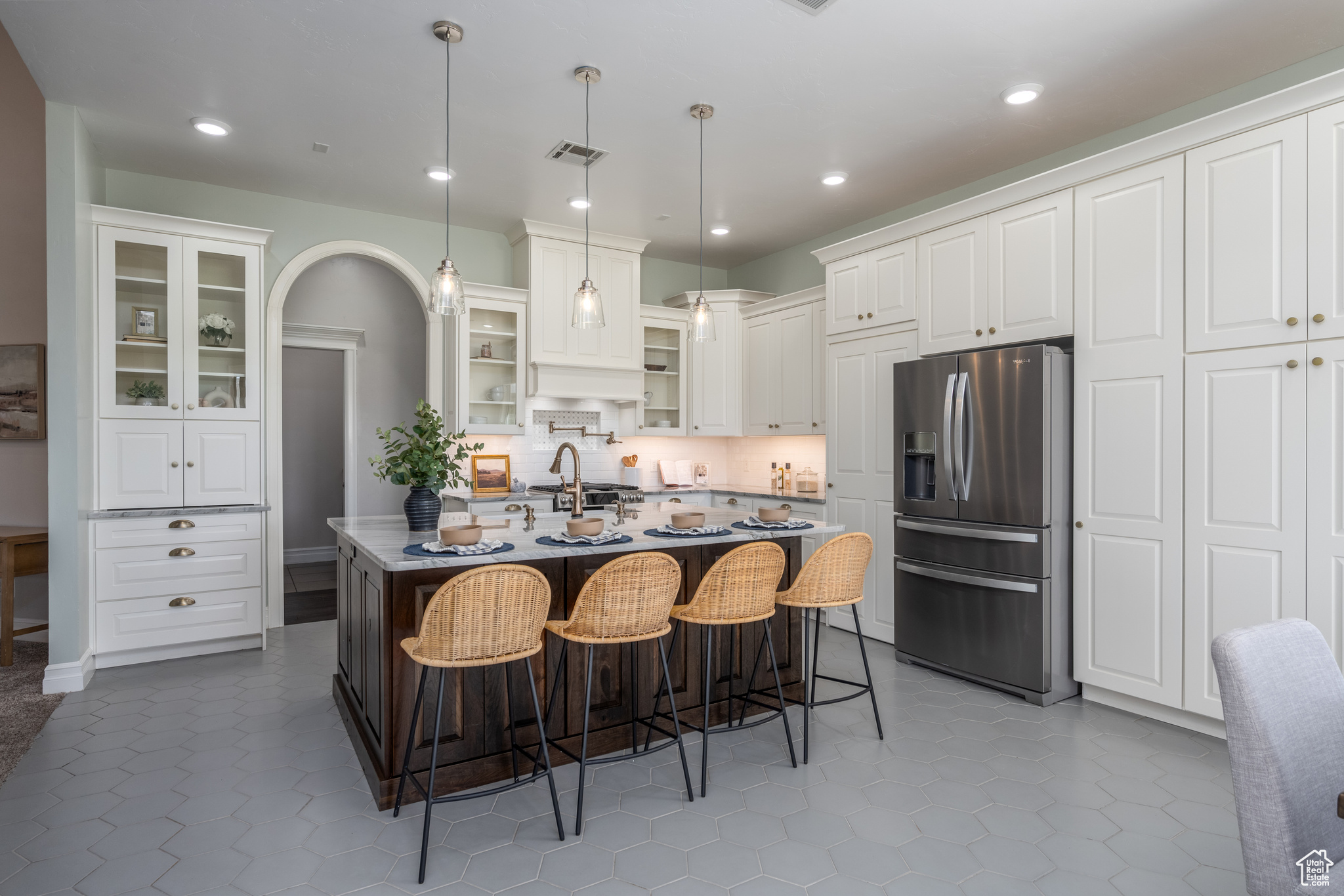 Kitchen featuring an island with sink, white cabinets, tasteful backsplash, and stainless steel fridge with ice dispenser