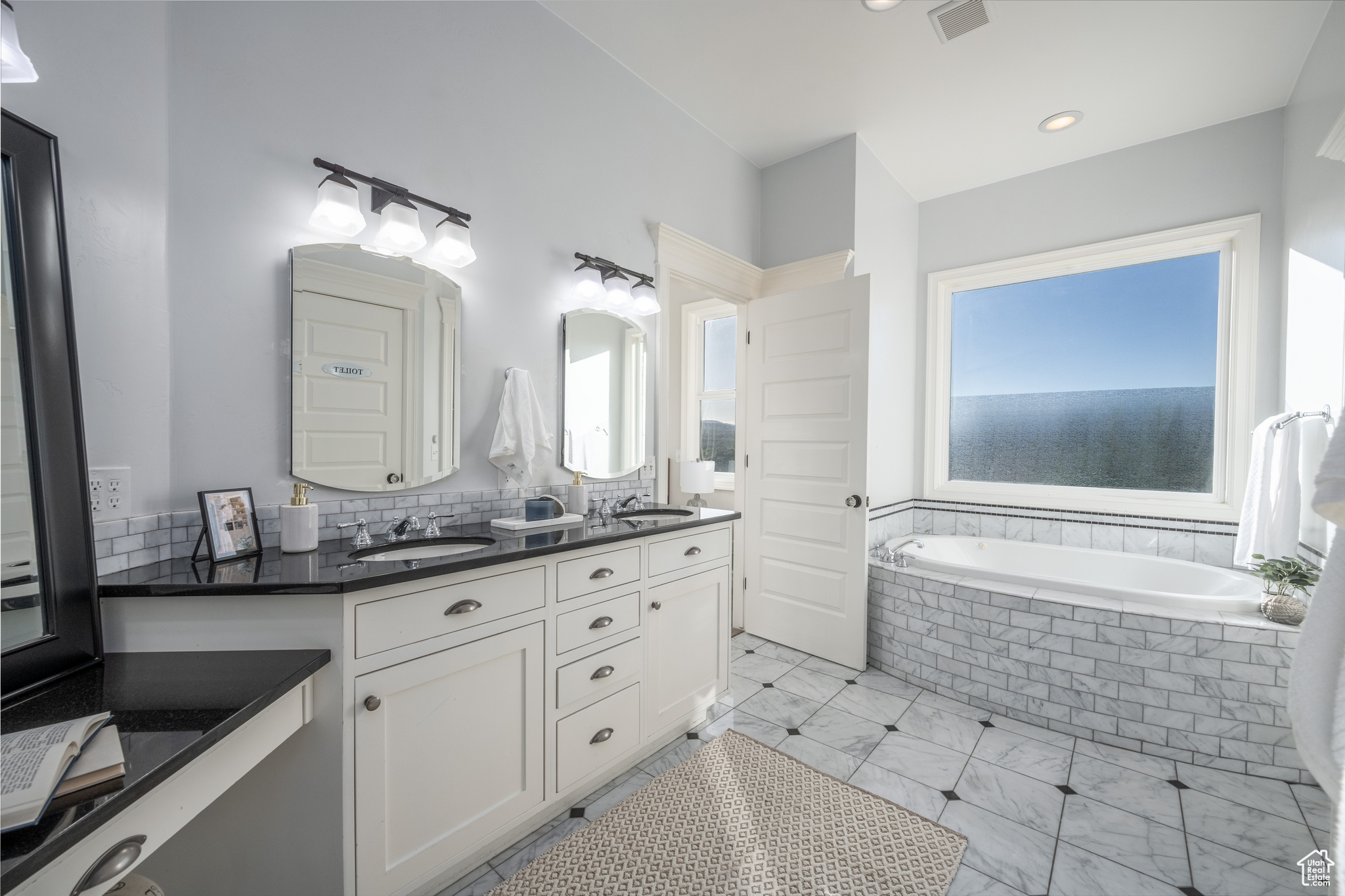 Bathroom with double sink, tile floors, plenty of natural light, and vanity with extensive cabinet space