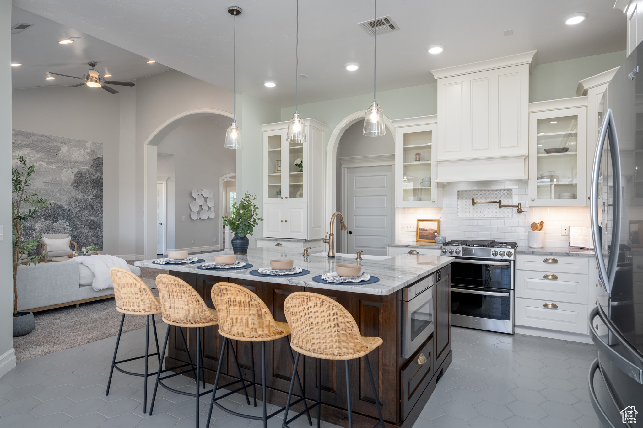 Kitchen with white cabinetry, tile flooring, stainless steel appliances, an island with sink, and backsplash