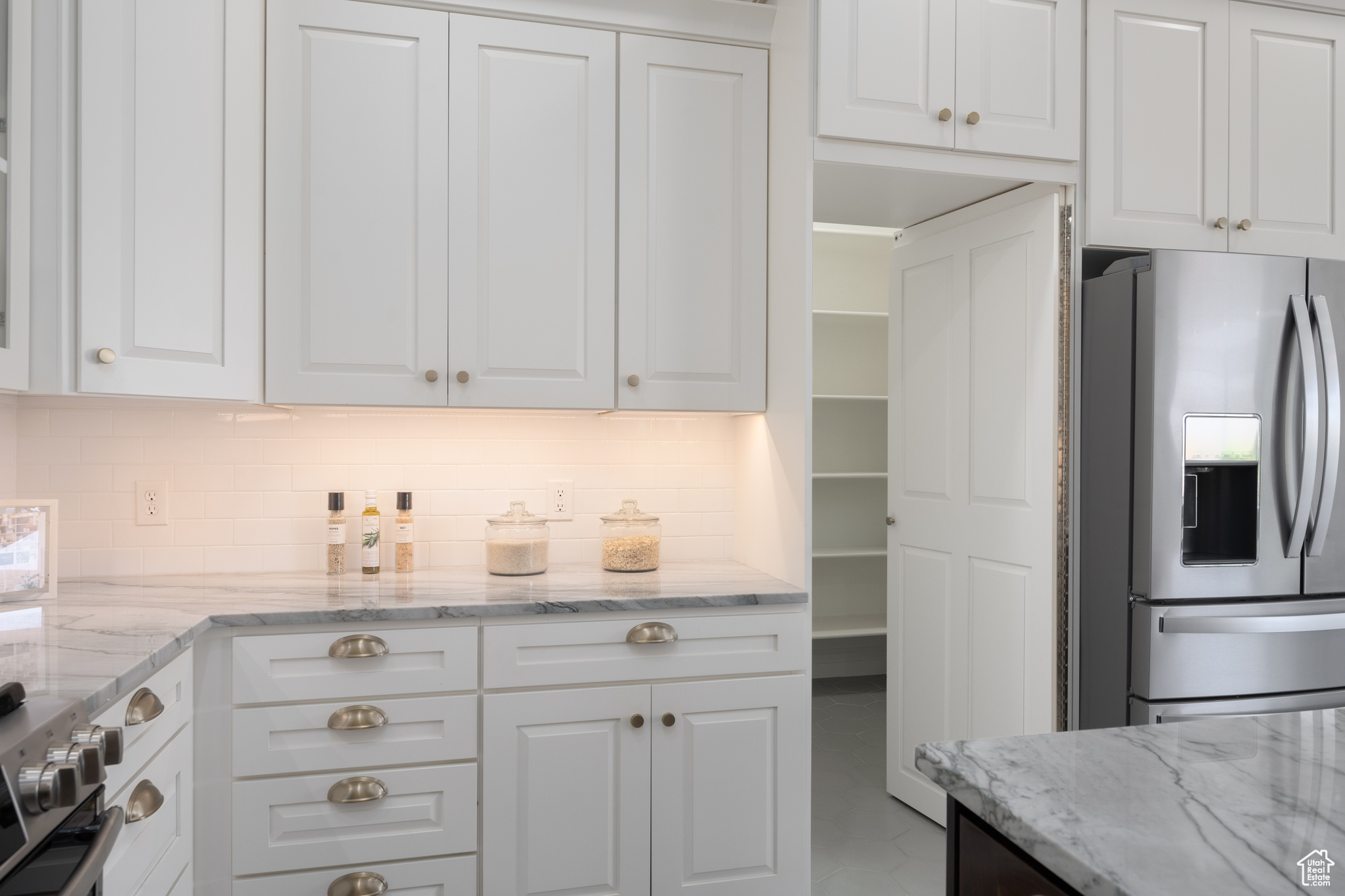 Kitchen with light stone countertops, white cabinets, backsplash, and appliances with stainless steel finishes