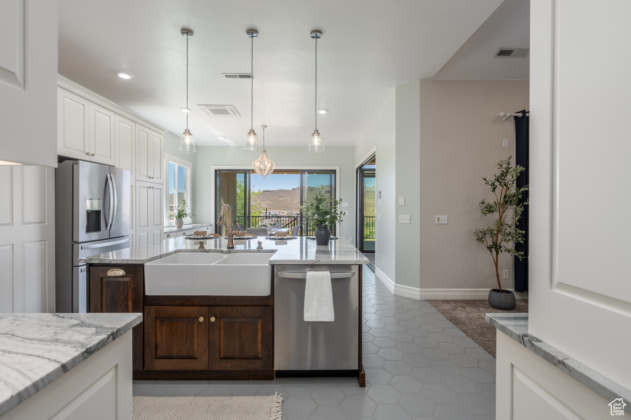 Kitchen featuring stainless steel appliances, tile flooring, light stone countertops, an island with sink, and sink