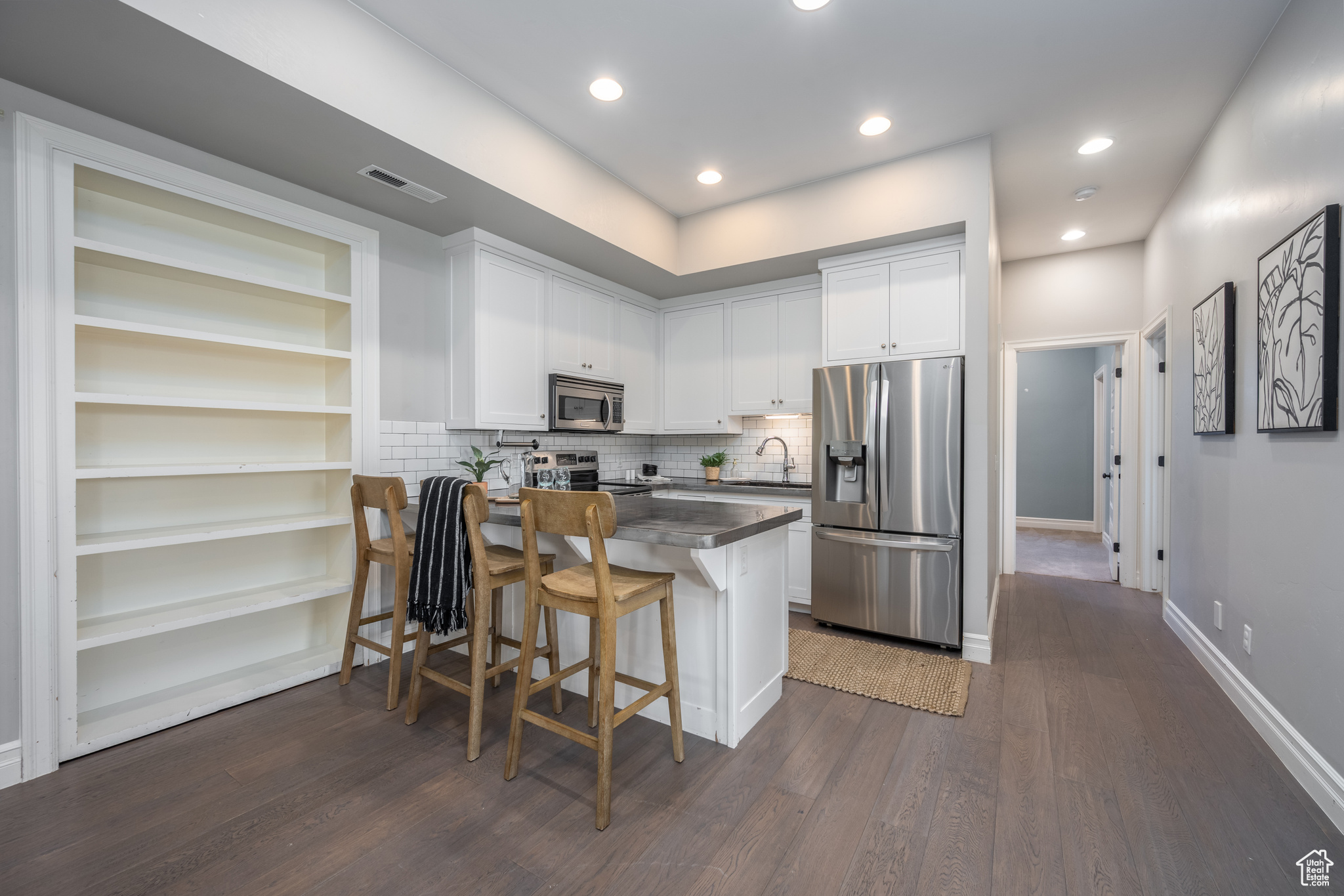 Kitchen with dark hardwood / wood-style flooring, kitchen peninsula, white cabinets, a breakfast bar, and appliances with stainless steel finishes