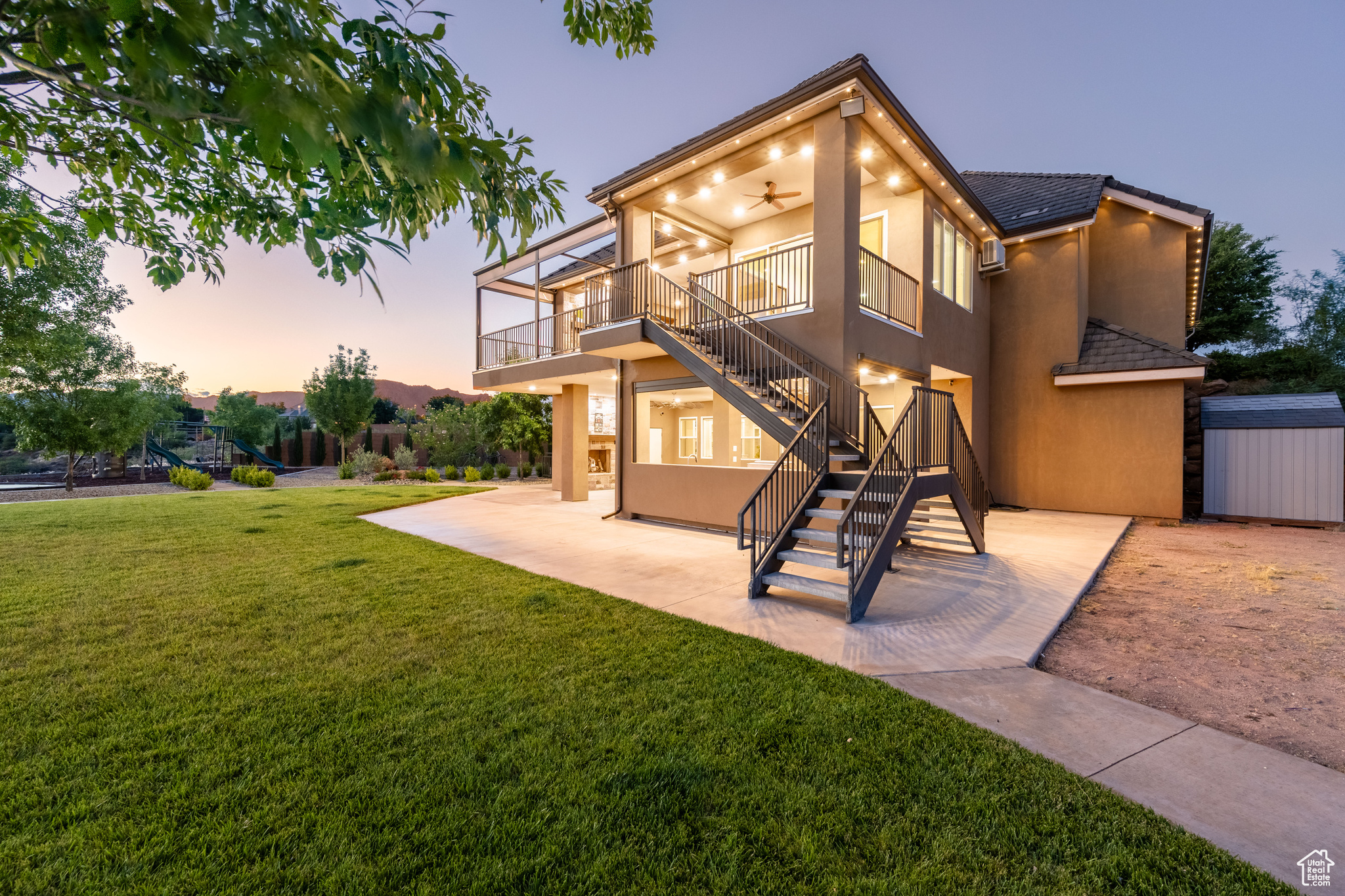 Back house at dusk featuring a patio, ceiling fan, a shed, and a lawn