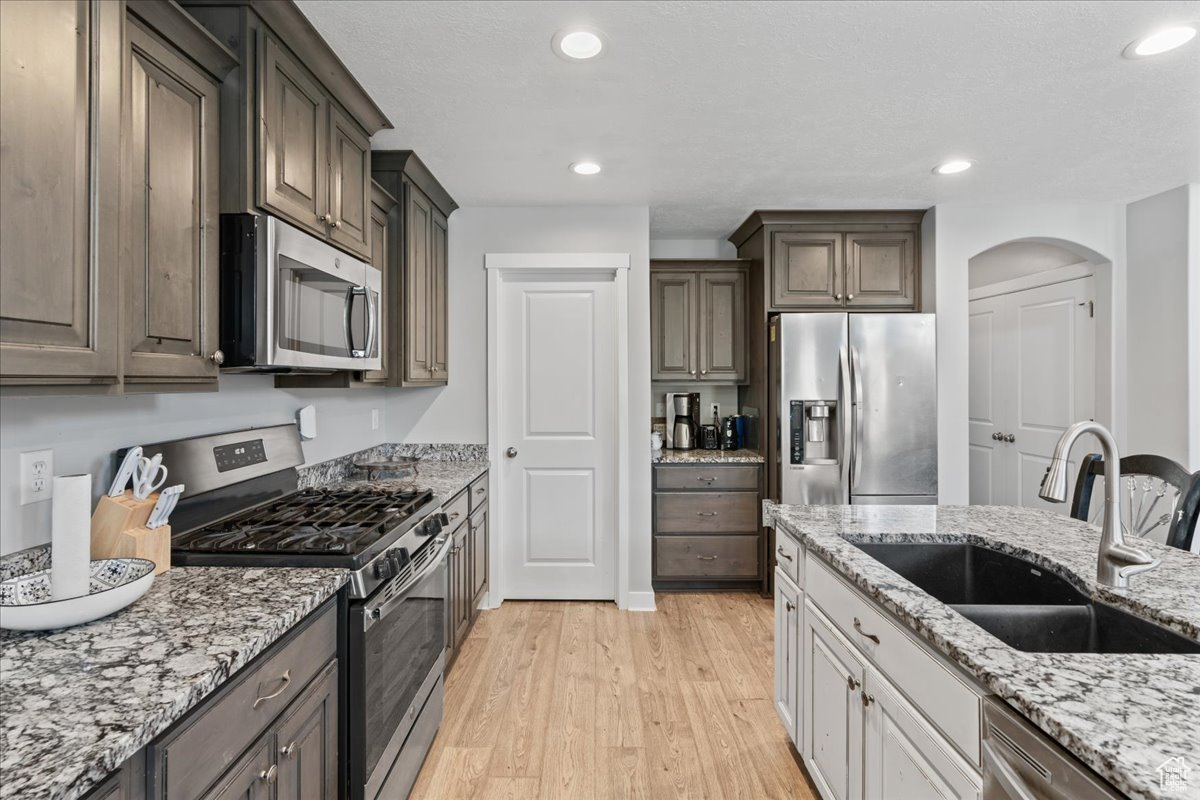 Kitchen with appliances with stainless steel finishes, sink, light stone counters, and light hardwood / wood-style flooring