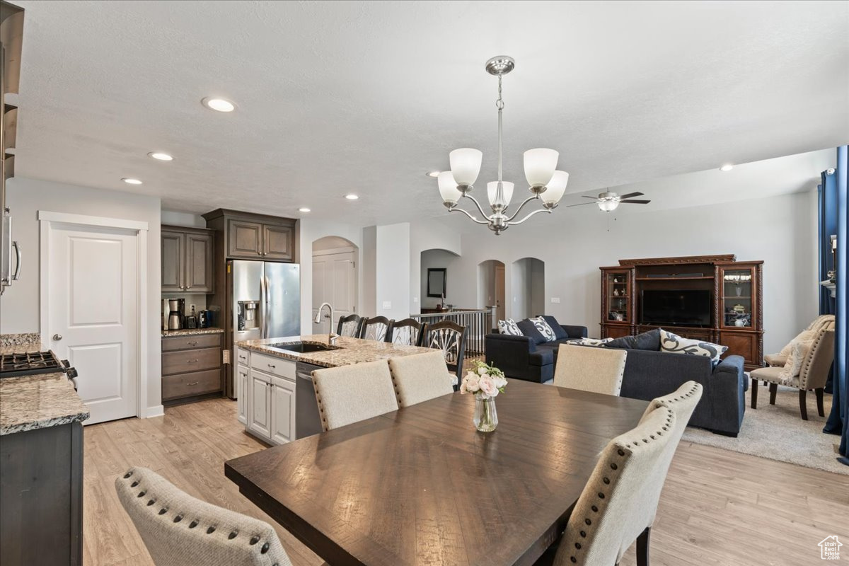 Dining space with sink, light hardwood / wood-style floors, and ceiling fan with notable chandelier