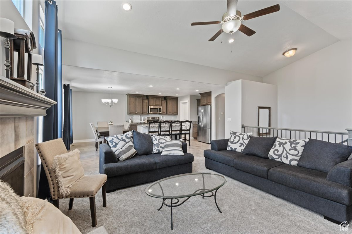 Carpeted living room with a fireplace and ceiling fan with notable chandelier