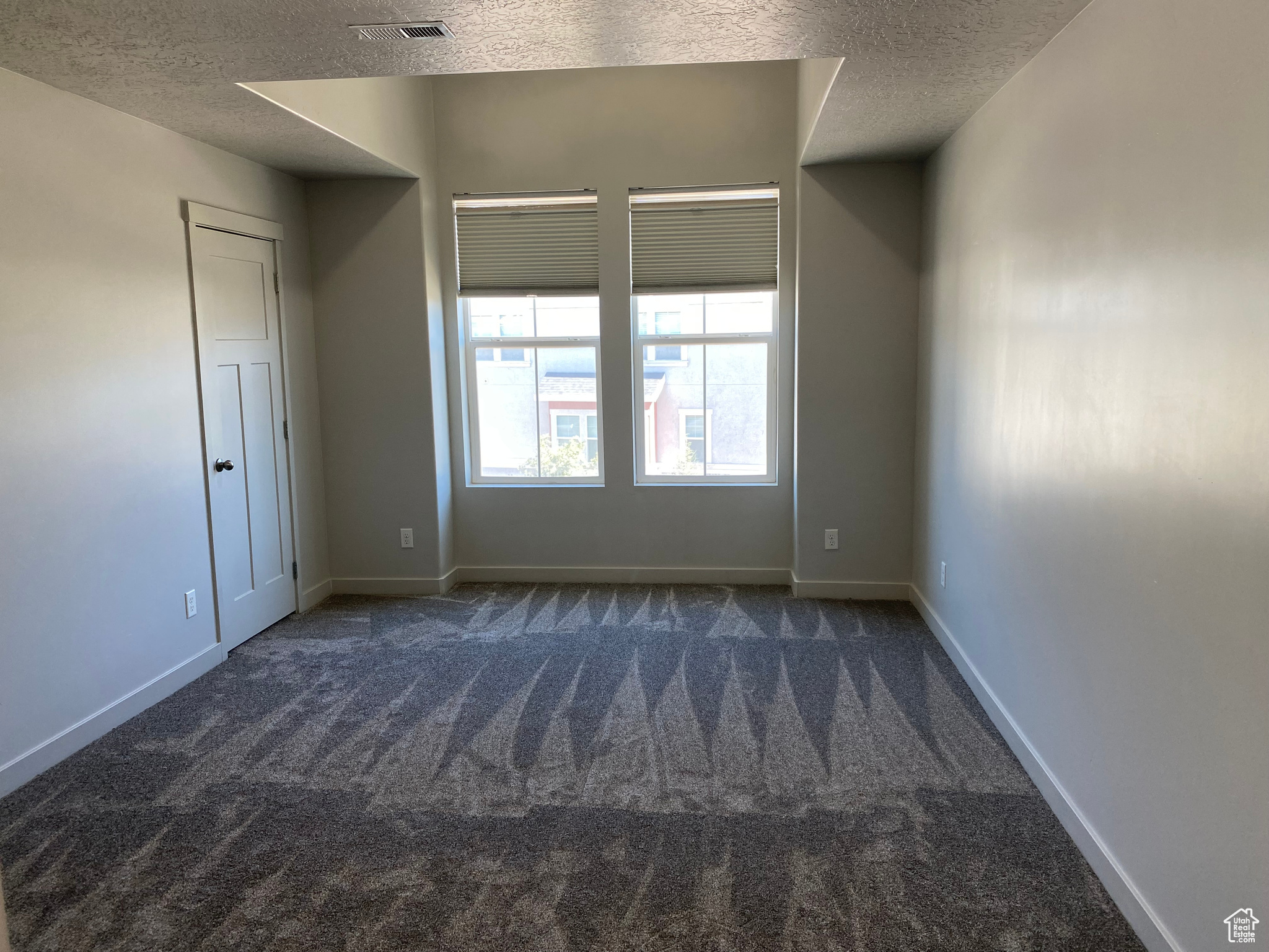 Empty room featuring dark colored carpet and a textured ceiling