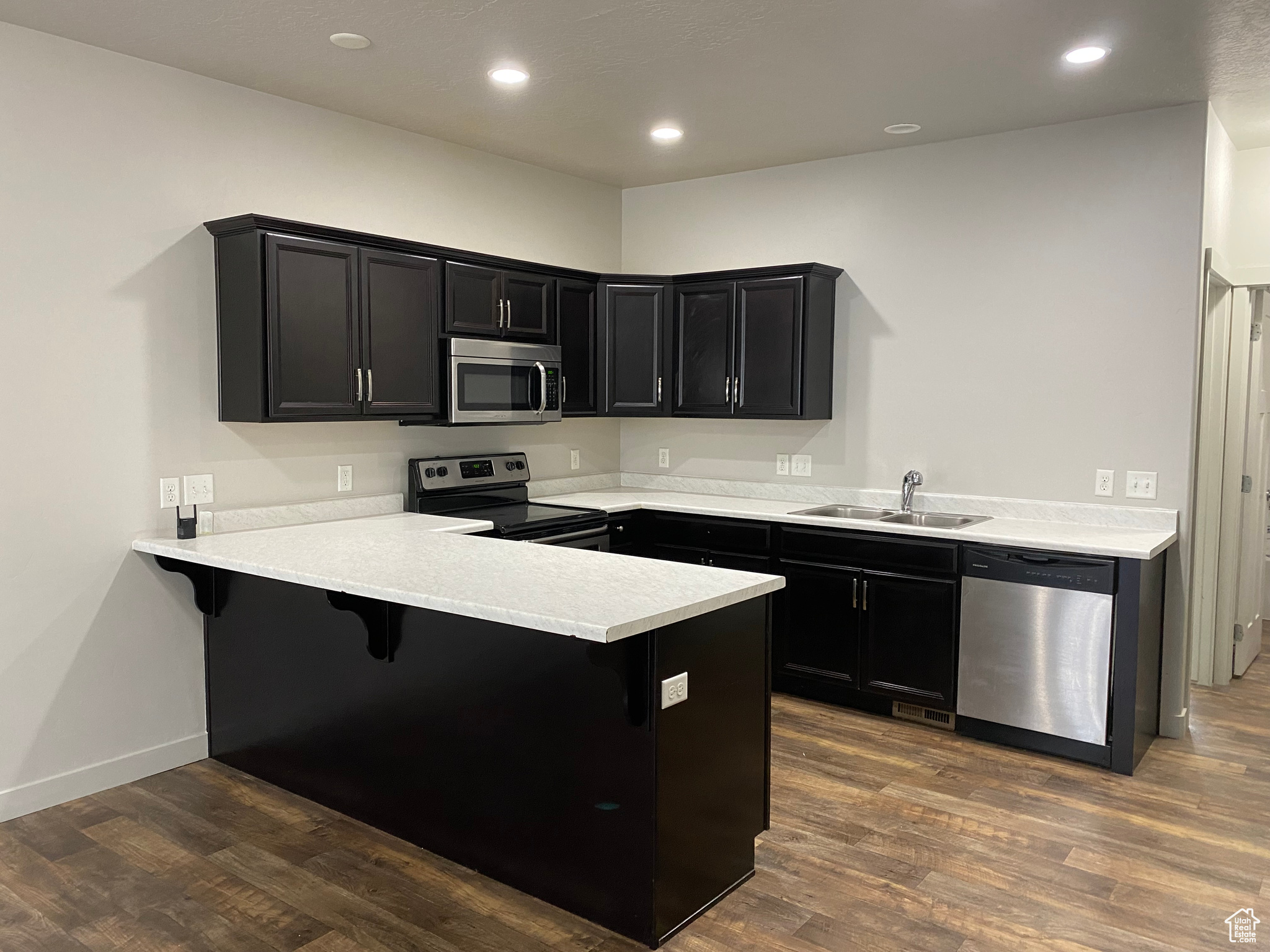 Kitchen featuring stainless steel appliances, dark wood-type flooring, kitchen peninsula, and a kitchen breakfast bar