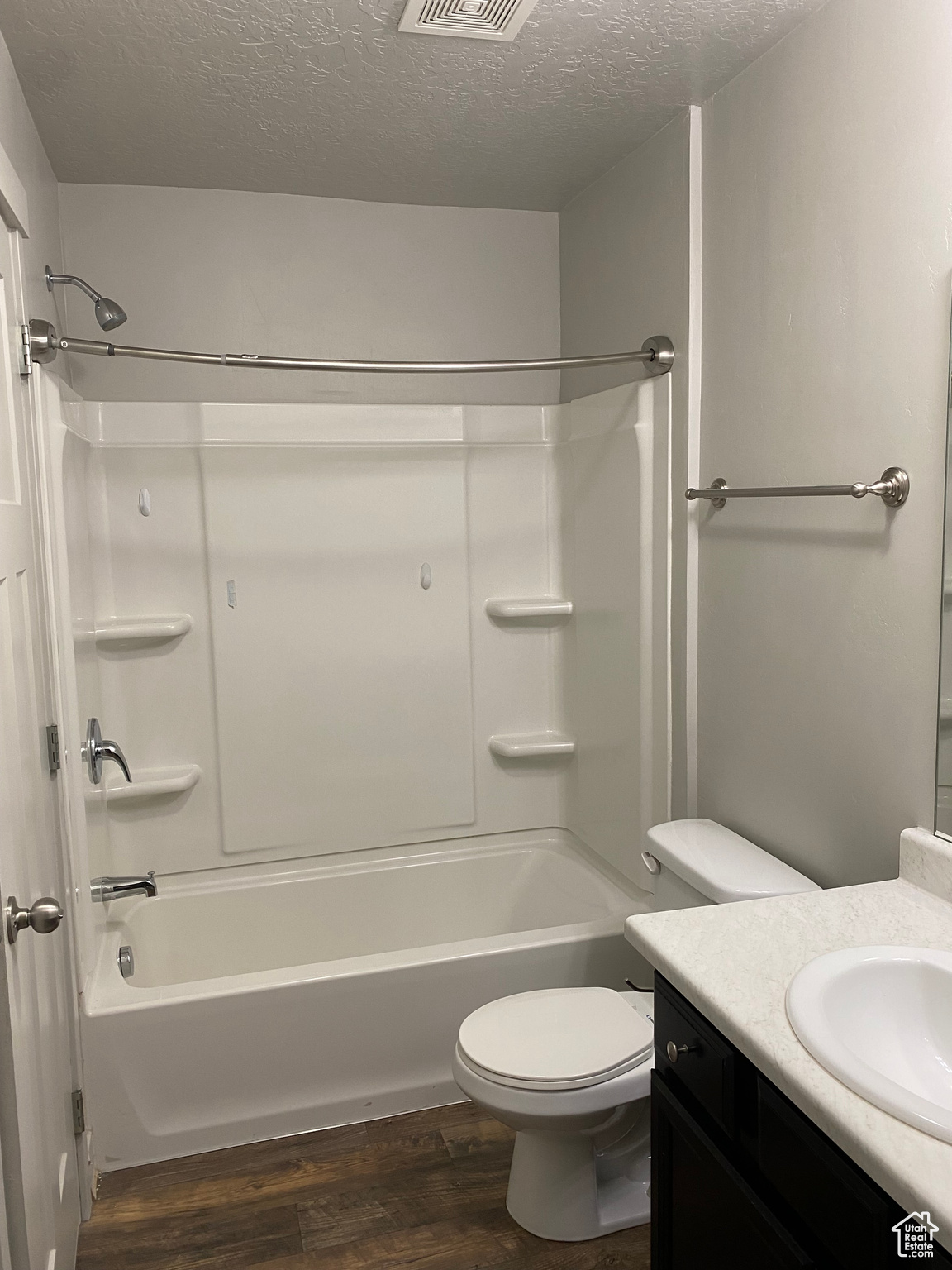 Full bathroom with vanity, wood-type flooring, a textured ceiling, shower / bathing tub combination, and toilet