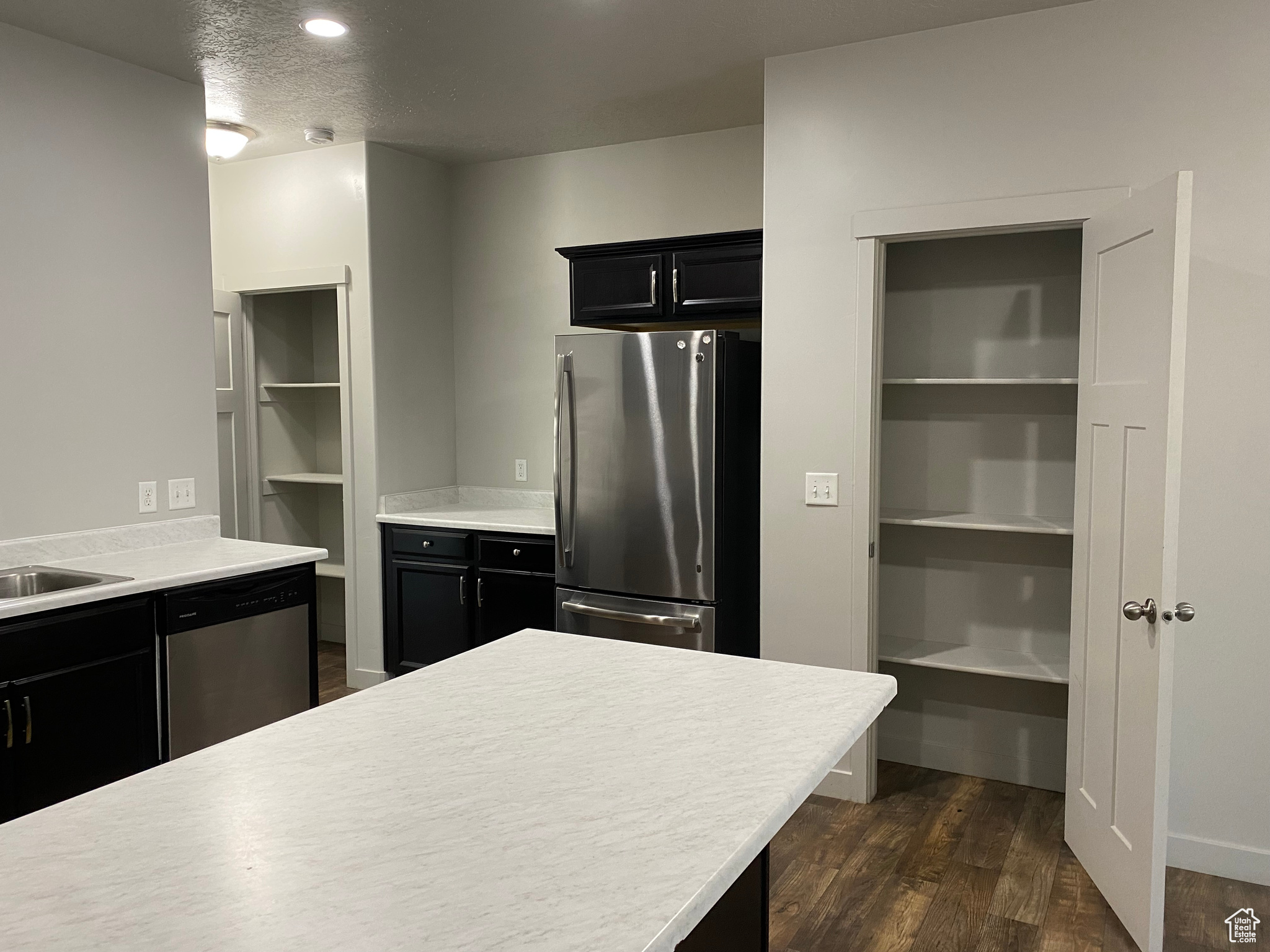 Kitchen with a textured ceiling, appliances with stainless steel finishes, and dark wood-type flooring