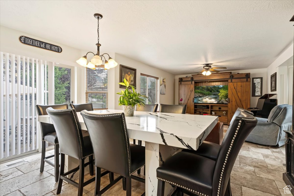 Tiled dining room featuring ceiling fan with notable chandelier and a barn door