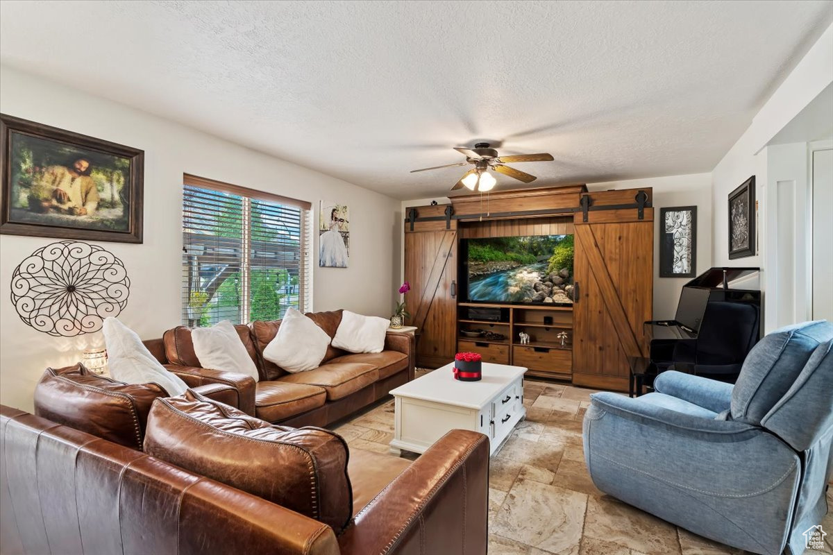 Living room with light tile patterned flooring, a textured ceiling, ceiling fan, and a barn door