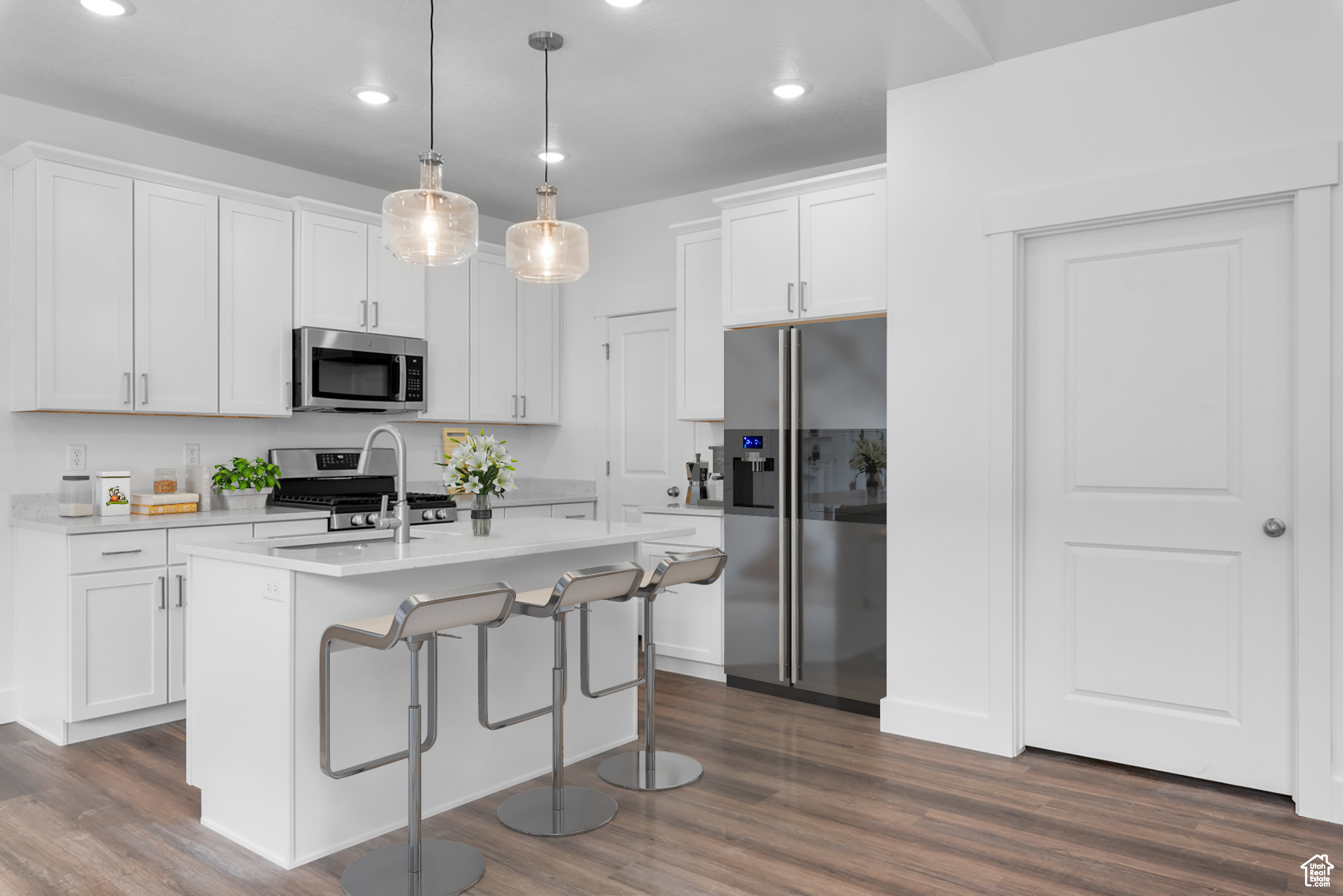 Kitchen with appliances with stainless steel finishes, hanging light fixtures, an island with sink, and dark hardwood / wood-style flooring